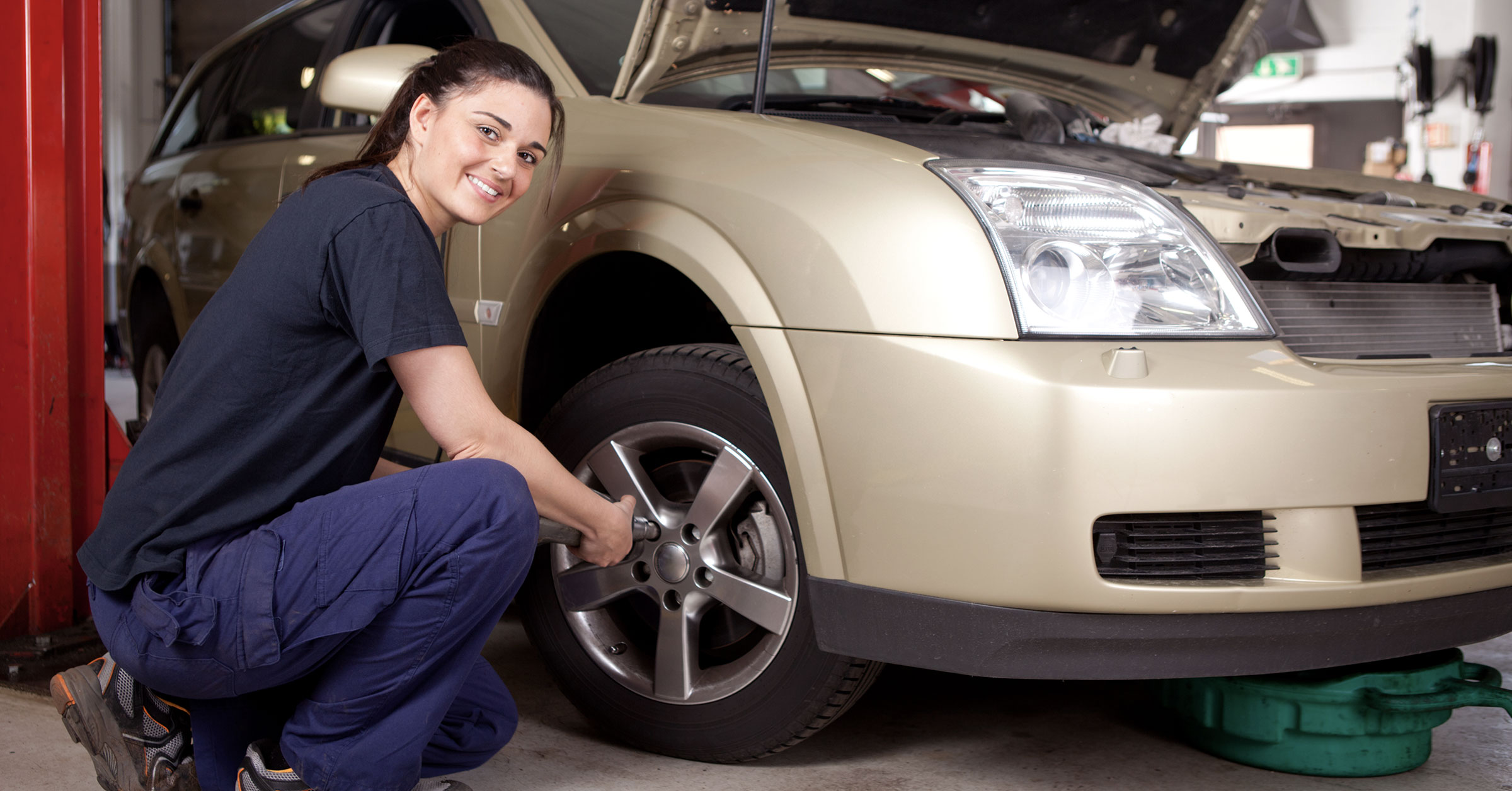 A photo of a female mechanic tightening the bolts of a car wheel in the garage.