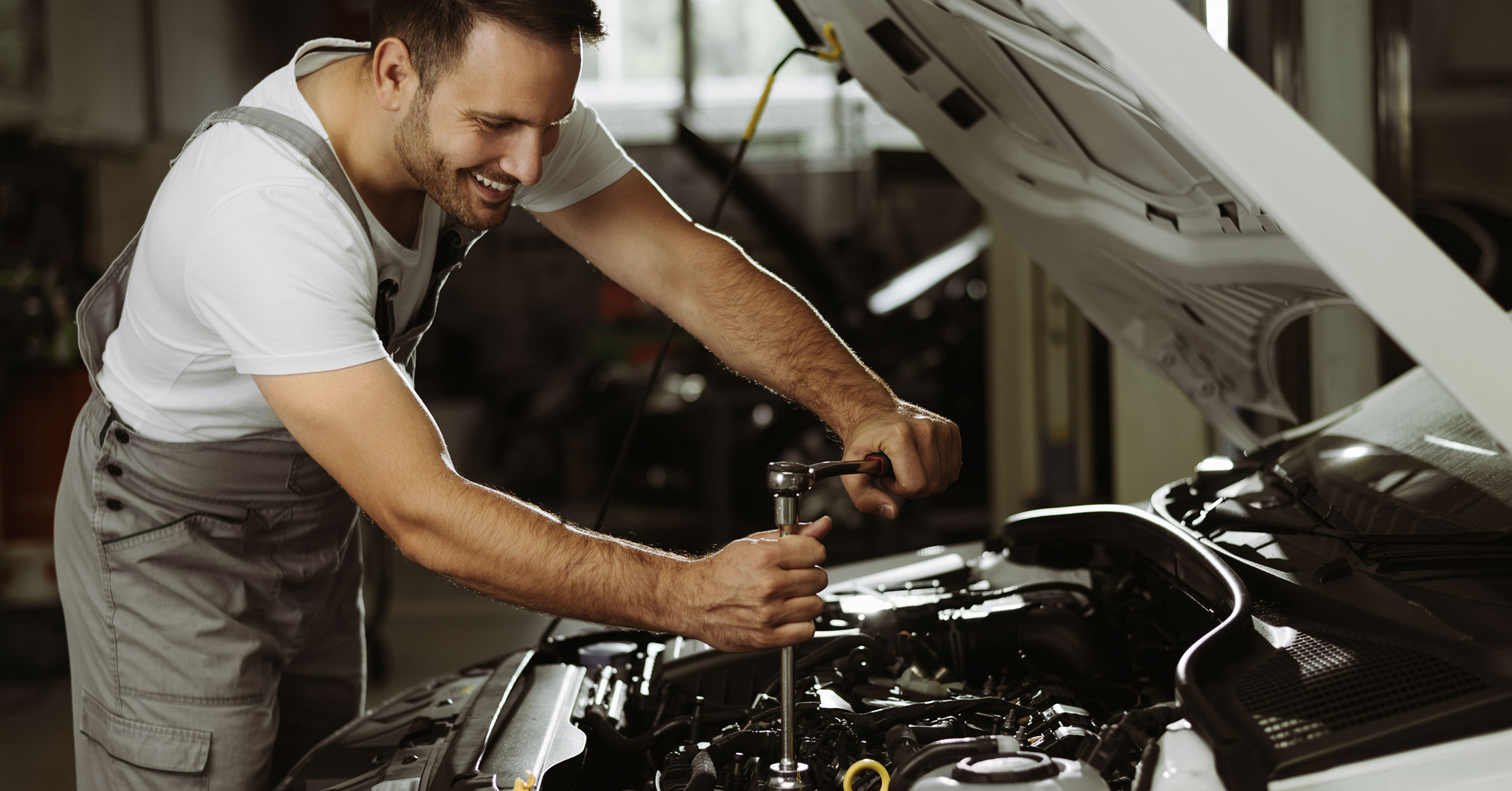 An image of a mechanic under a car hood, making repairs on the engine using the right tools