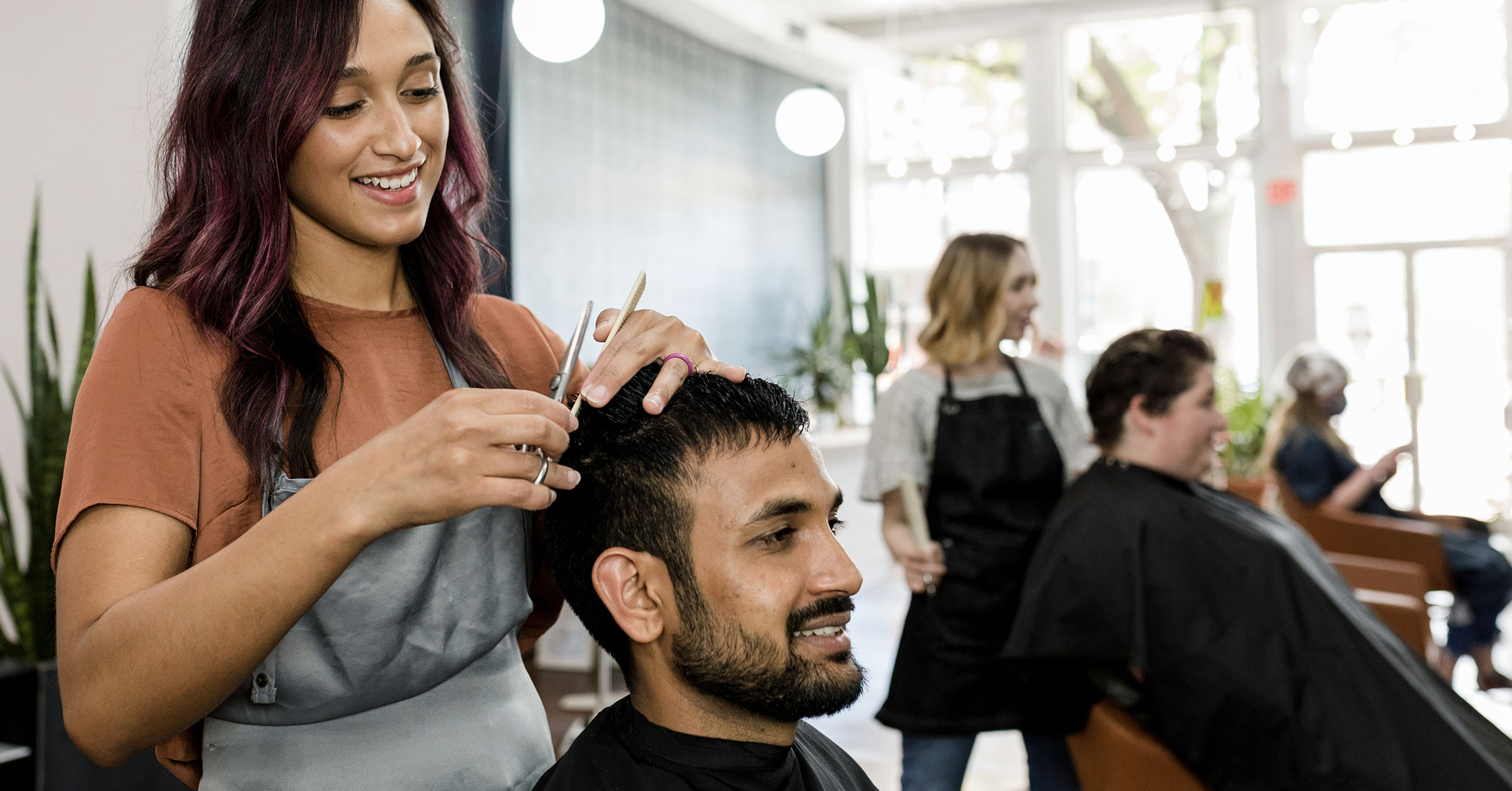 An image of a female barber trimming the hair of her client in a vibrant barber shop