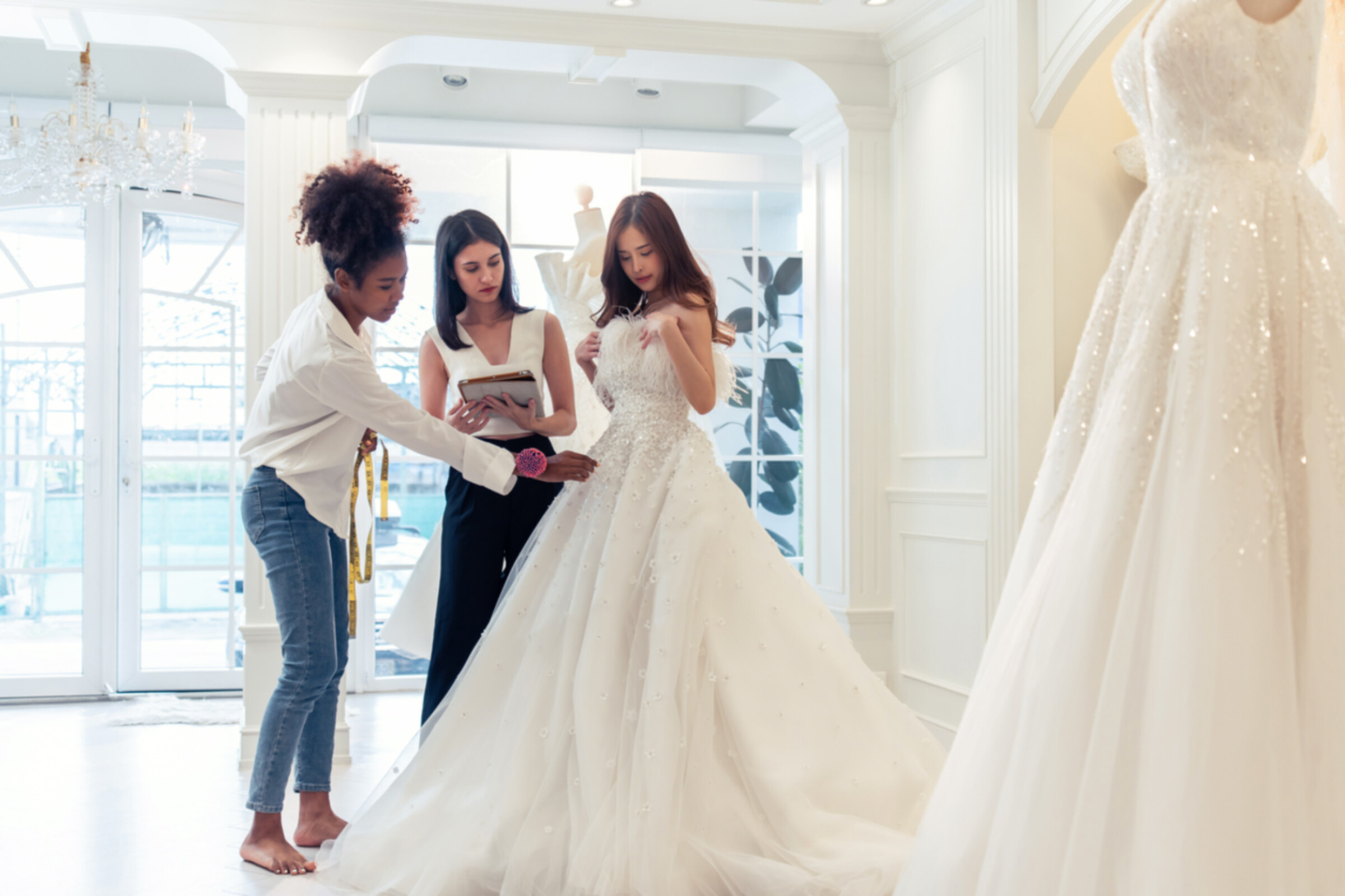 A bride-to-be fitting on a wedding dress and discussing it with her wedding planner and altier.