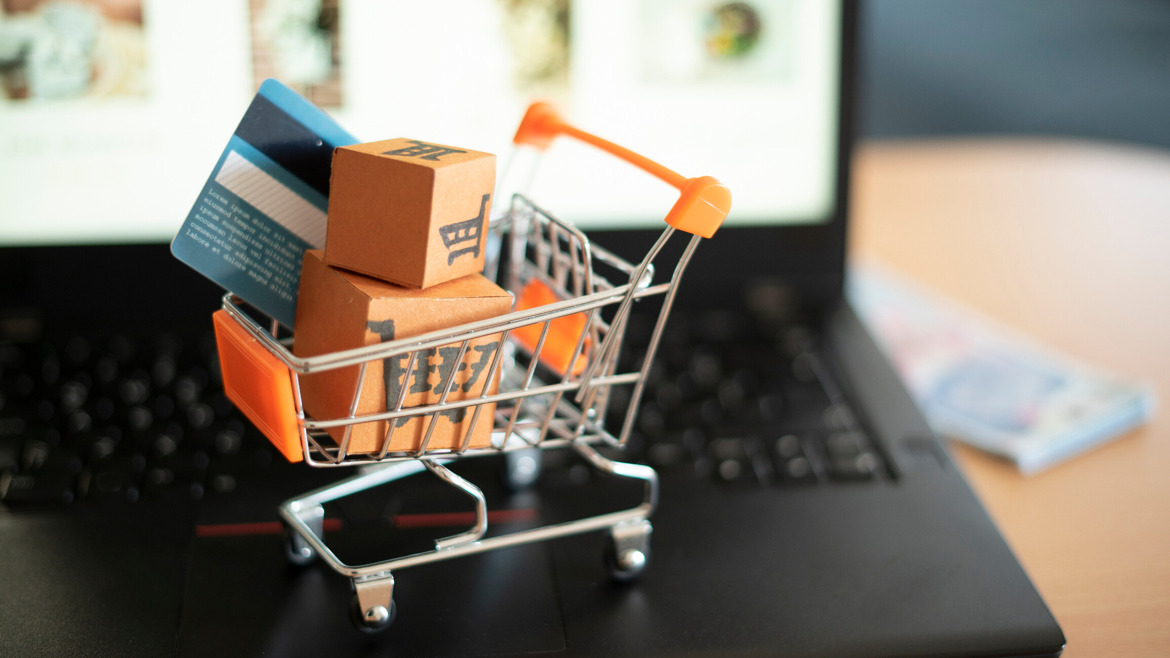 A miniature shopping cart on a laptop symbolizing online shopping.