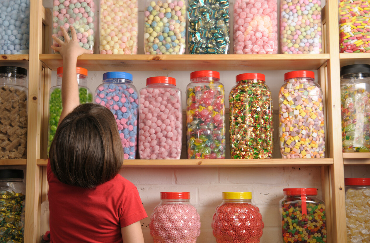 kid reaching for a jar in a shelf full of candies