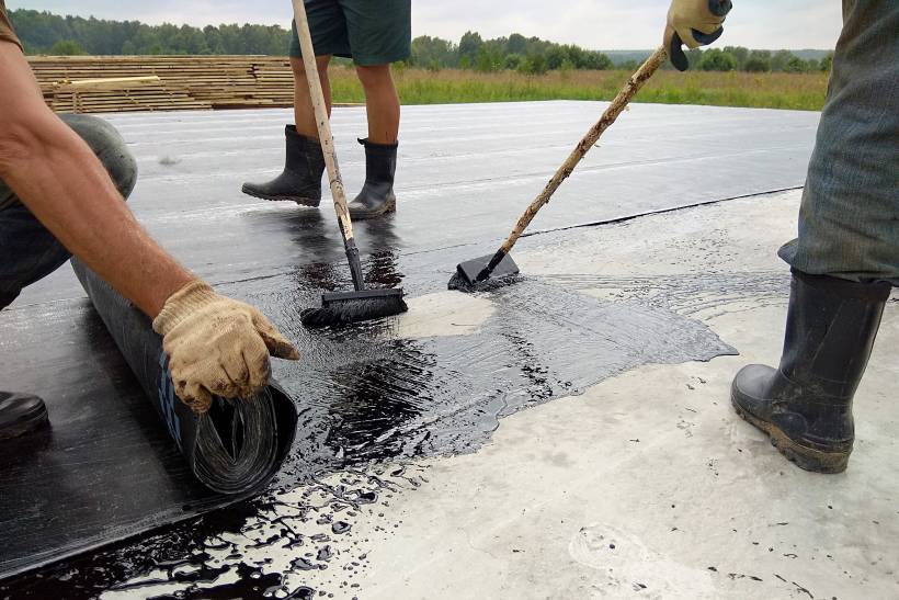 three people laying bitumen on a road