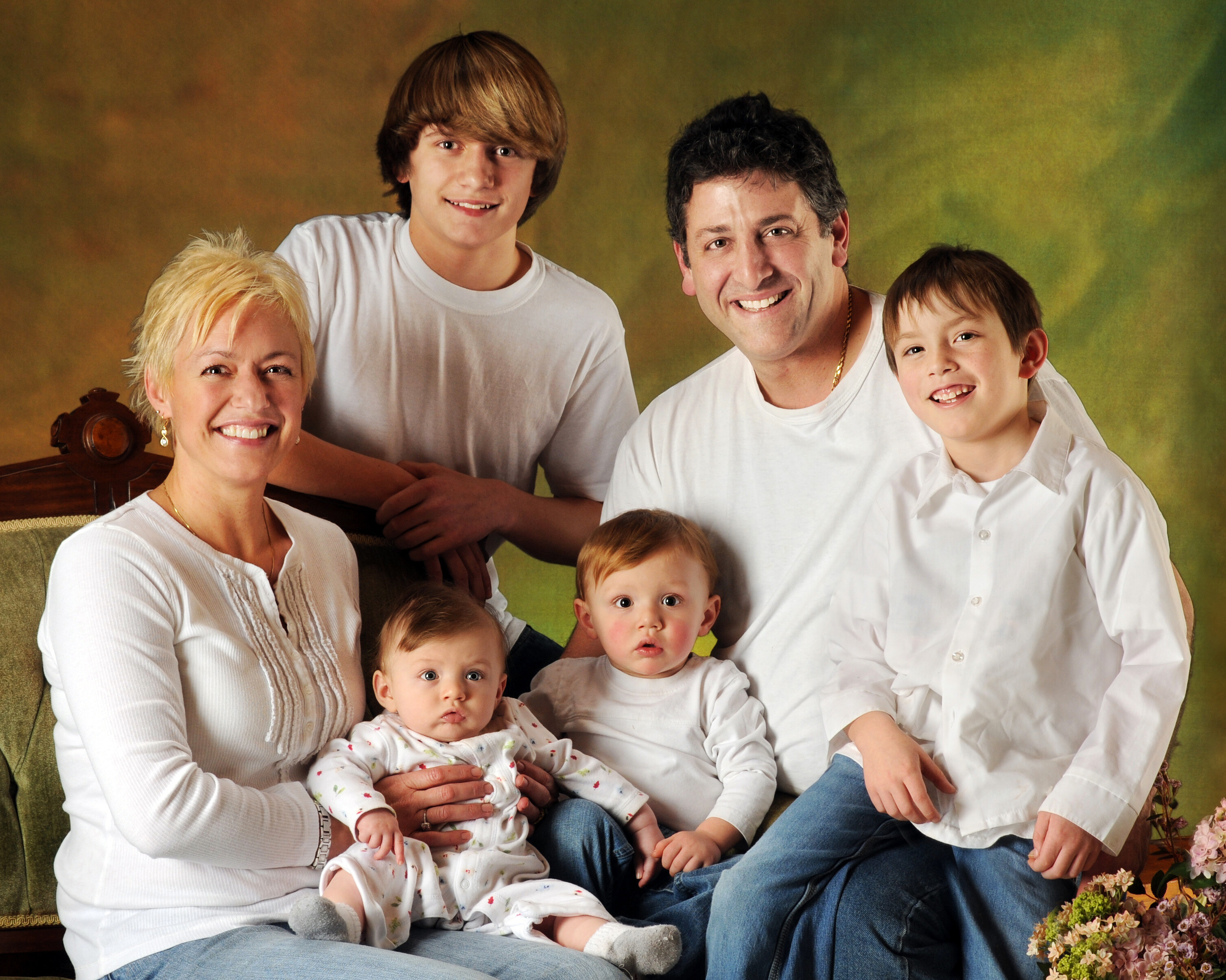 A family portrait composed of a dad, mom, and four sons. They are in a studio and dressed in white.