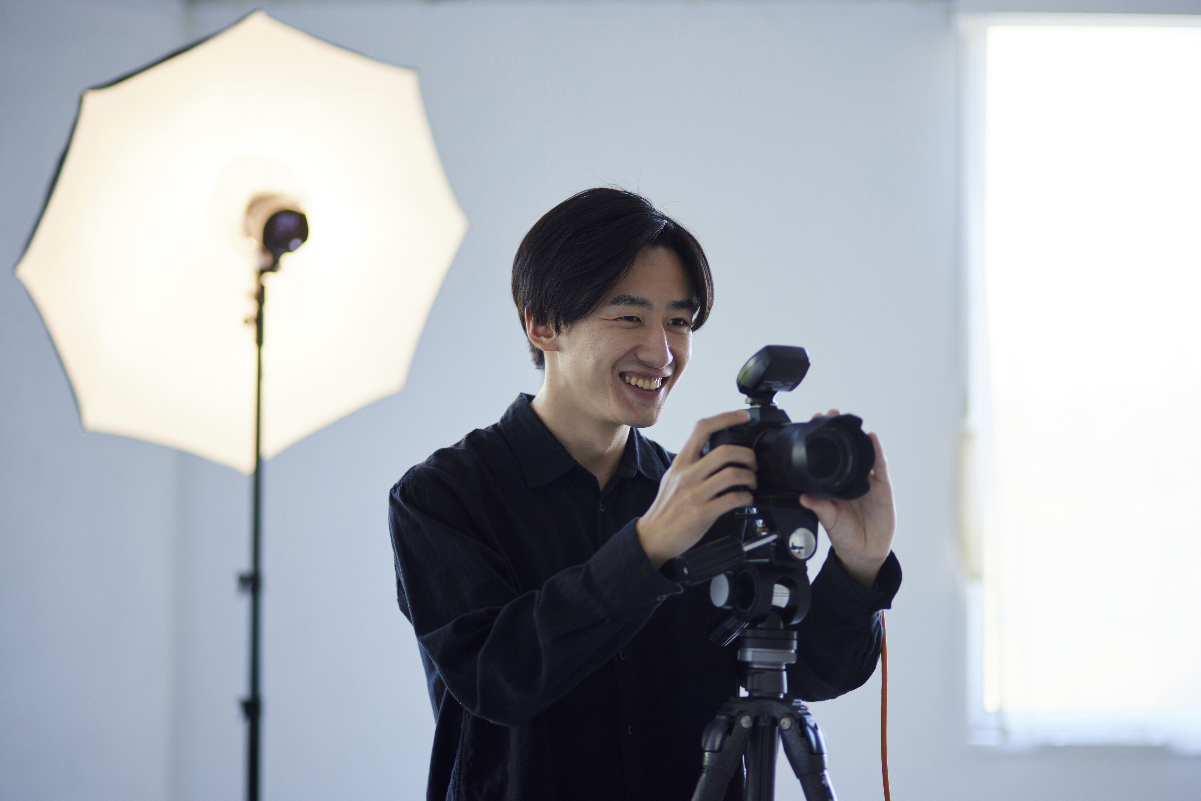 An Asian male photographer smiling as he takes pictures in a studio.