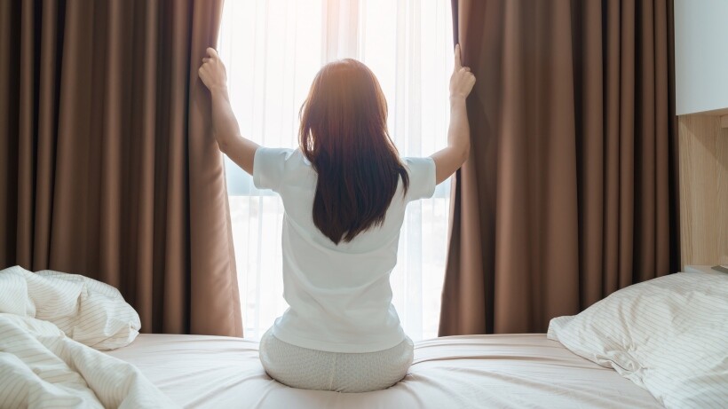 drapes vs curtains vs blinds - young adult female rising arms and looking to her window with drapes