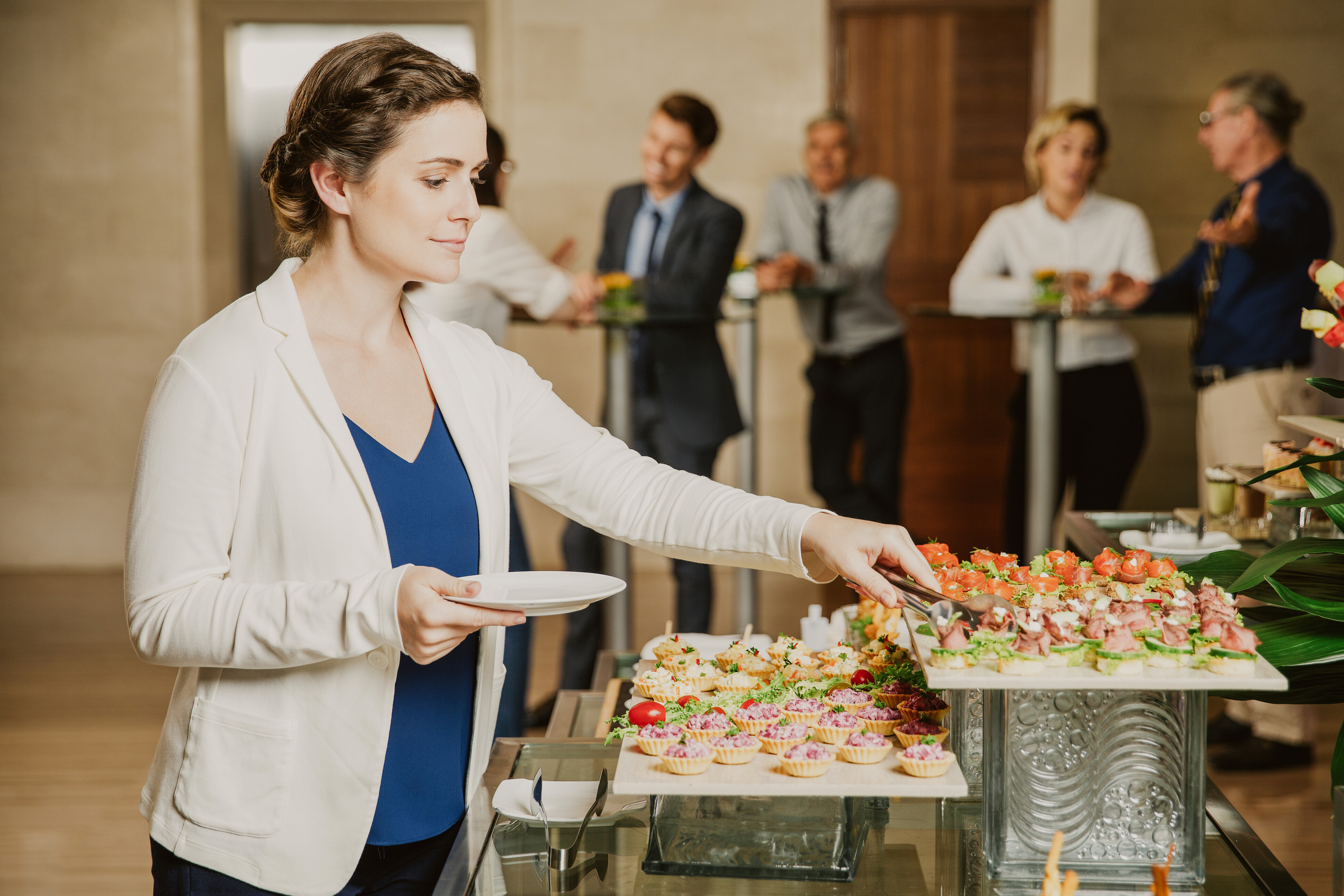 A woman in a blue shirt and and white jacket getting finger food from a caterer.