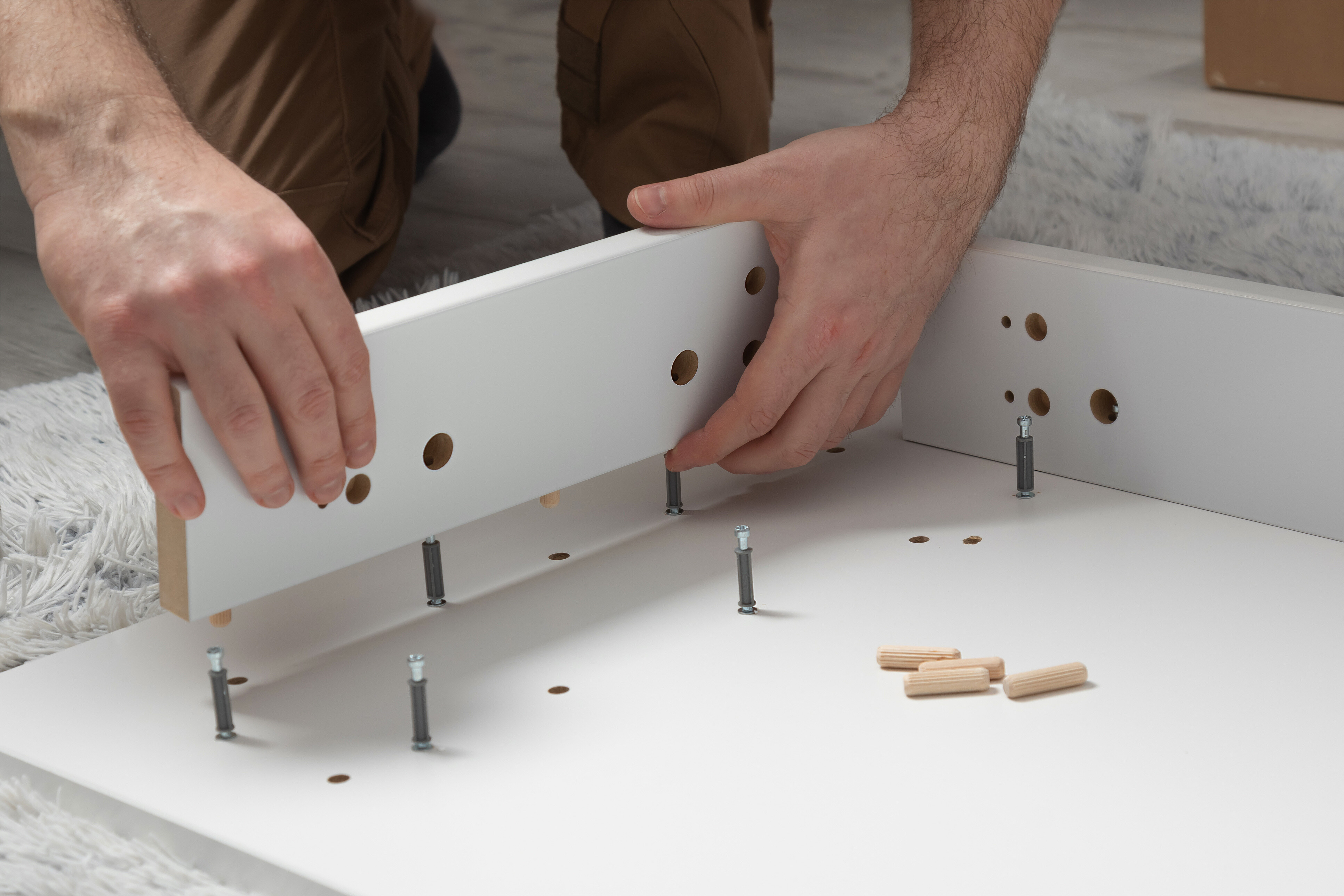 A pair of hands being shown putting a table together on a white carpet.