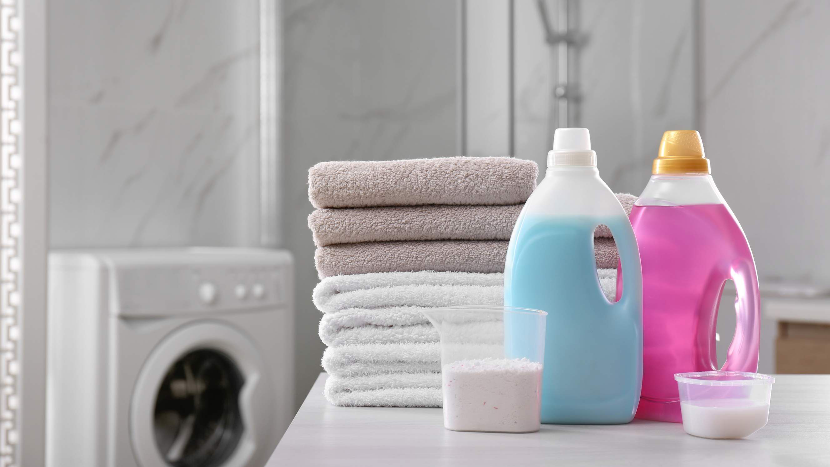 Fabric softener vs detergent - Detergent and fabric softener with stack of folded towels on white table in bathroom