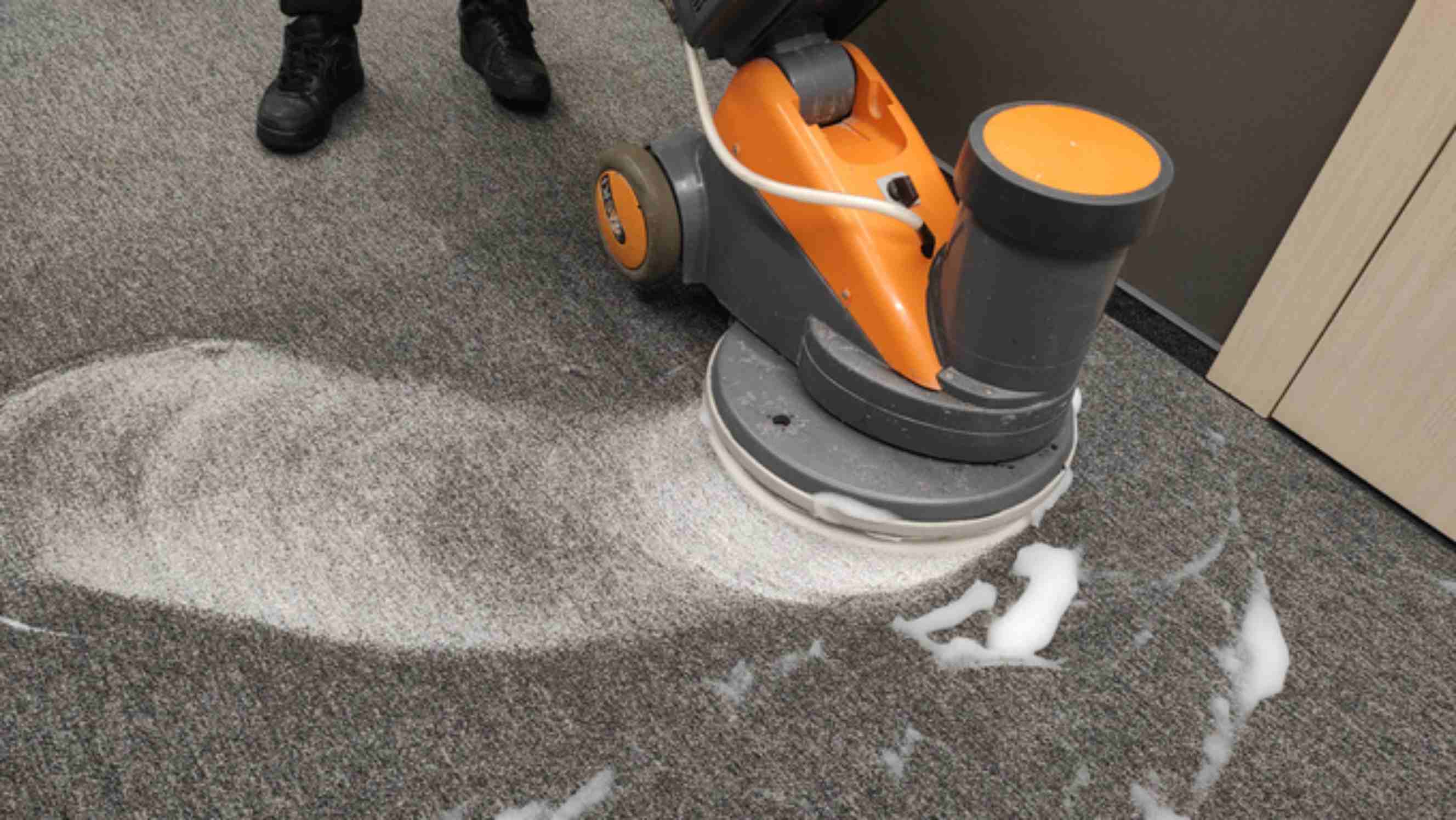 Steam cleaning carpets vs shampooing - a person cleaning a gray carpet using a carpet shampooer