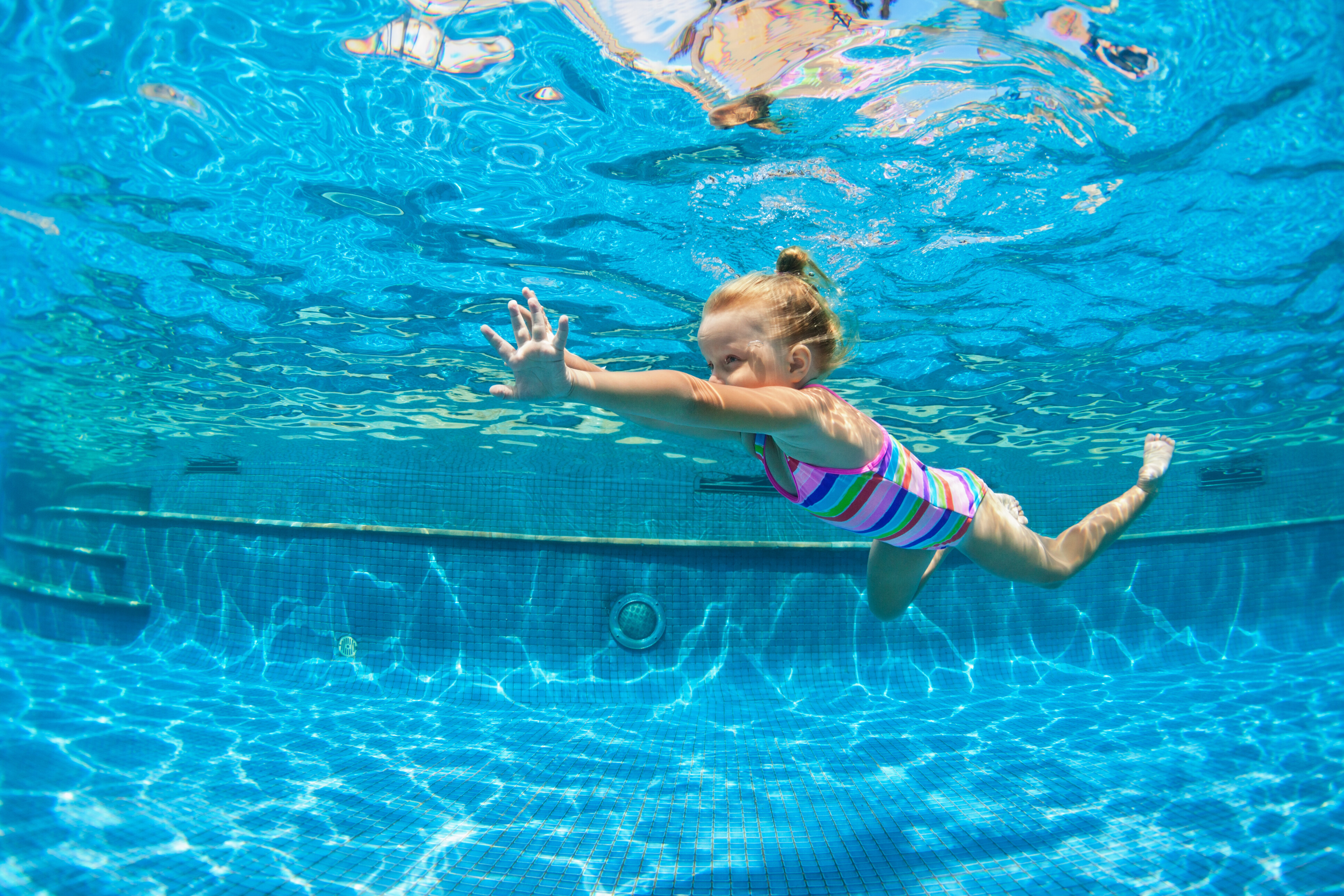 A child learns to swim, diving in a blue pool.