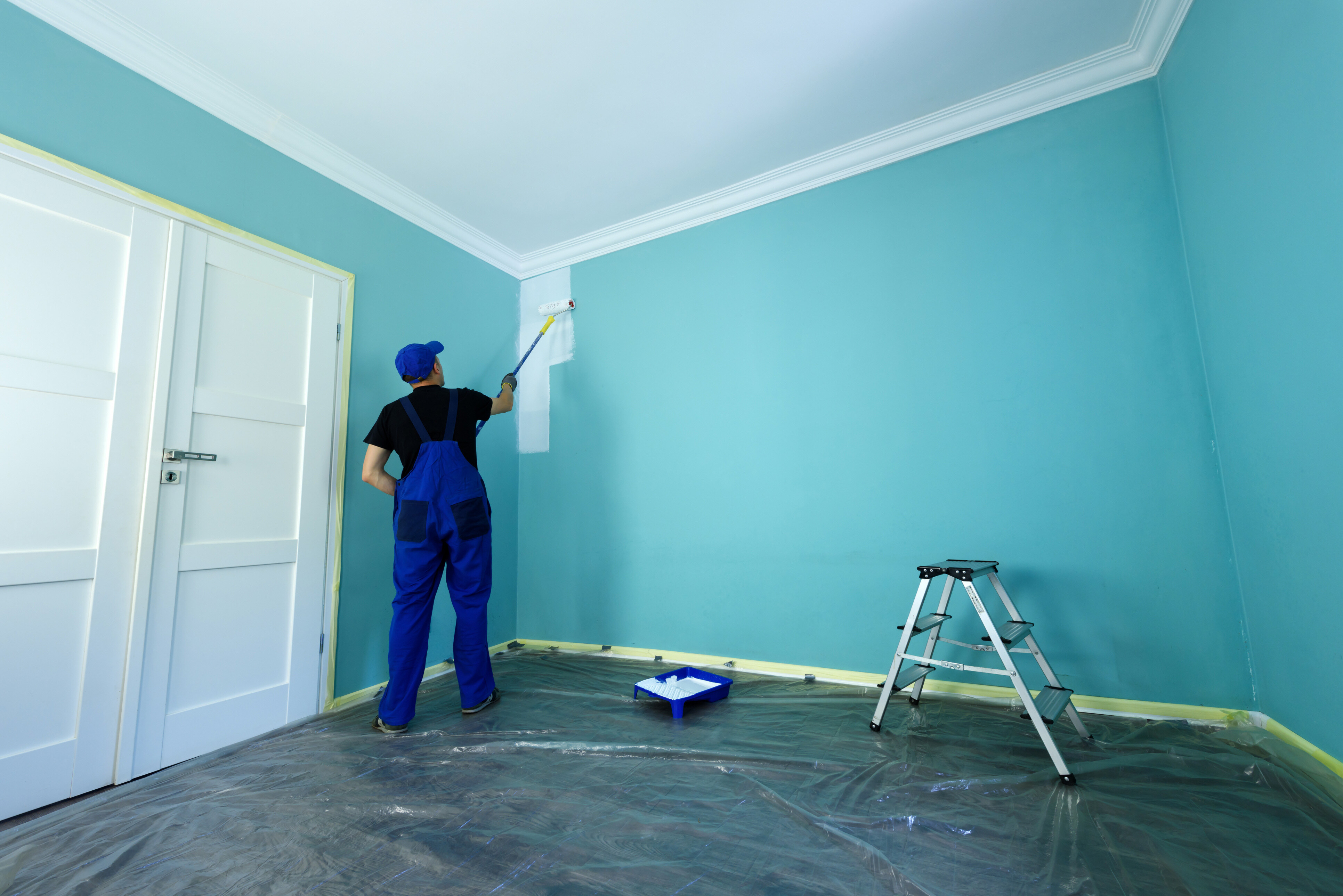 A professional painter wearing a blue jumpsuit paint the interior walls of a house.