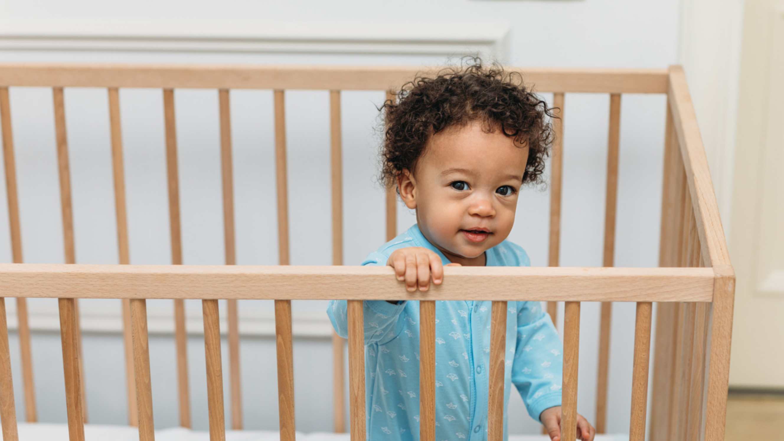 Bassinet vs cot - A smiling baby standing in a wooden cot