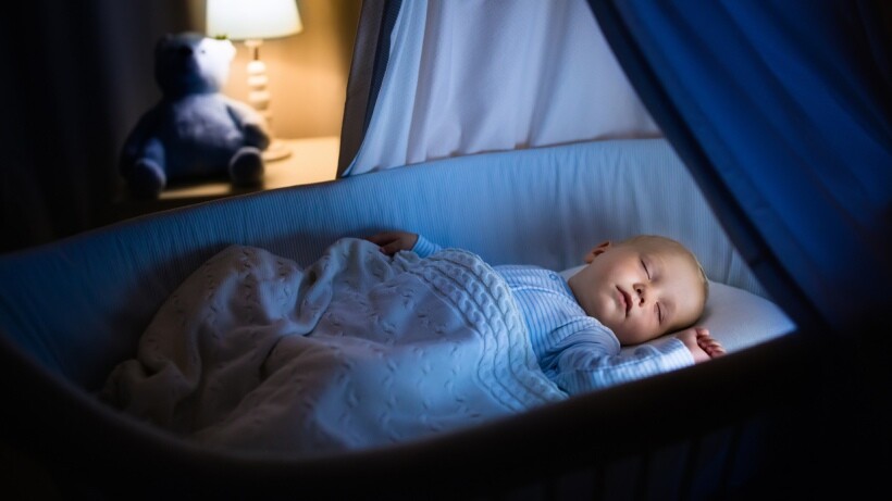 Bassinet vs cot - Adorable baby sleeping in blue bassinet with canopy at night
