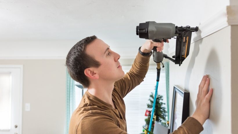 Nail gun vs staple gun - Black and grey nail gun used to install white wood crown moulding in own a home renovation