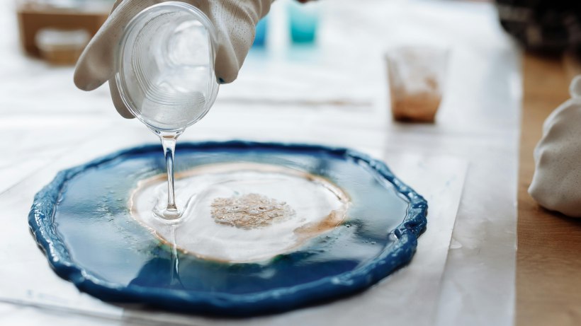 Polyester resin vs epoxy resin - A person wearing gloves carefully pours a clear polyester resin from a container Polyester resin vs epoxy resin - A person wearing gloves carefully pours a clear polyester resin from a container 