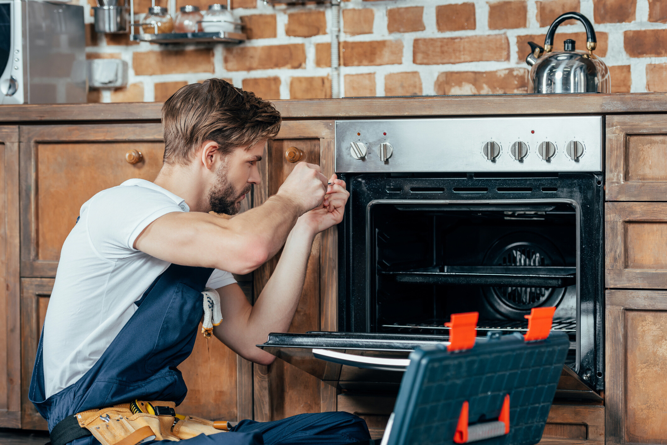 A professional worker making appliance repairs on an oven.