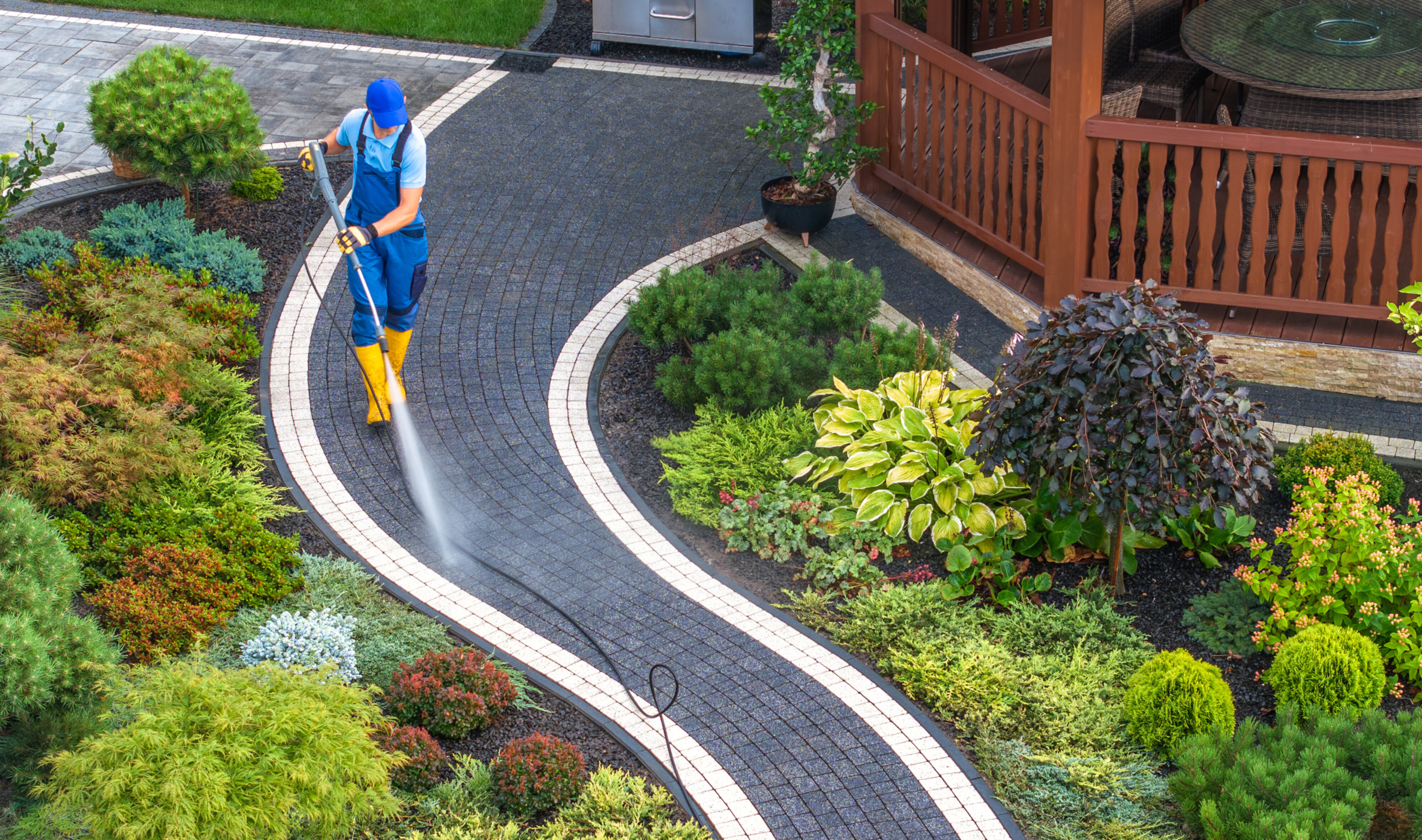 a professional cleaner using a high pressure washer to clean a walking path in a garden.