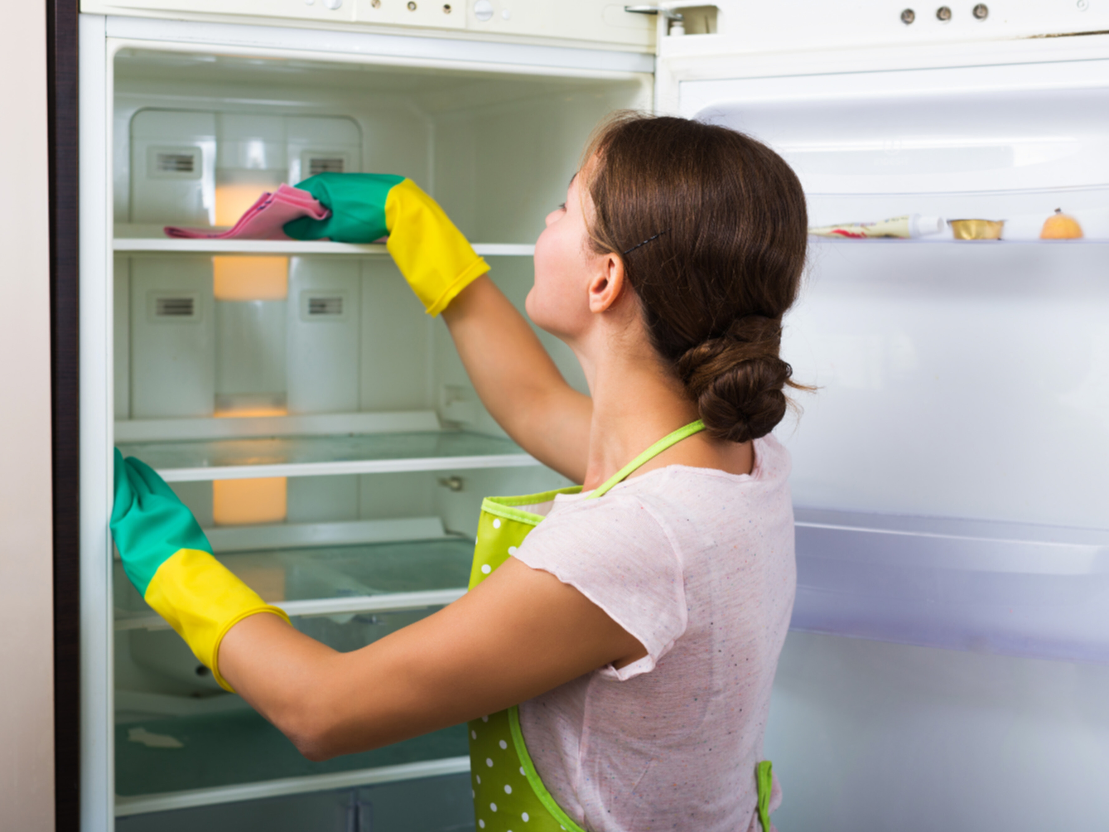 A caucasian woman thoroughly cleaning the inside of a fridge.