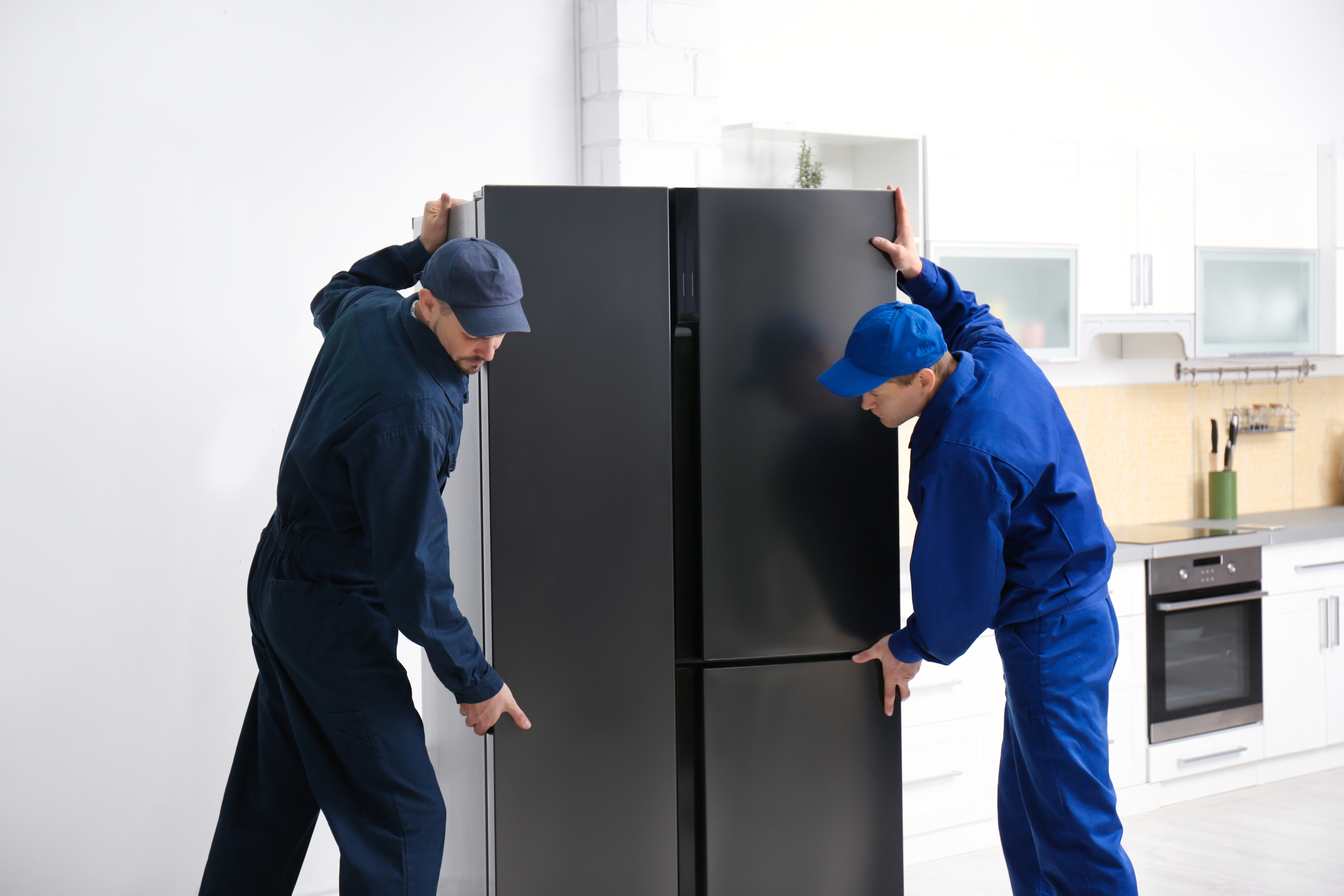 A pair of handymen carying a double door fridge to the kitchen in order to install it.