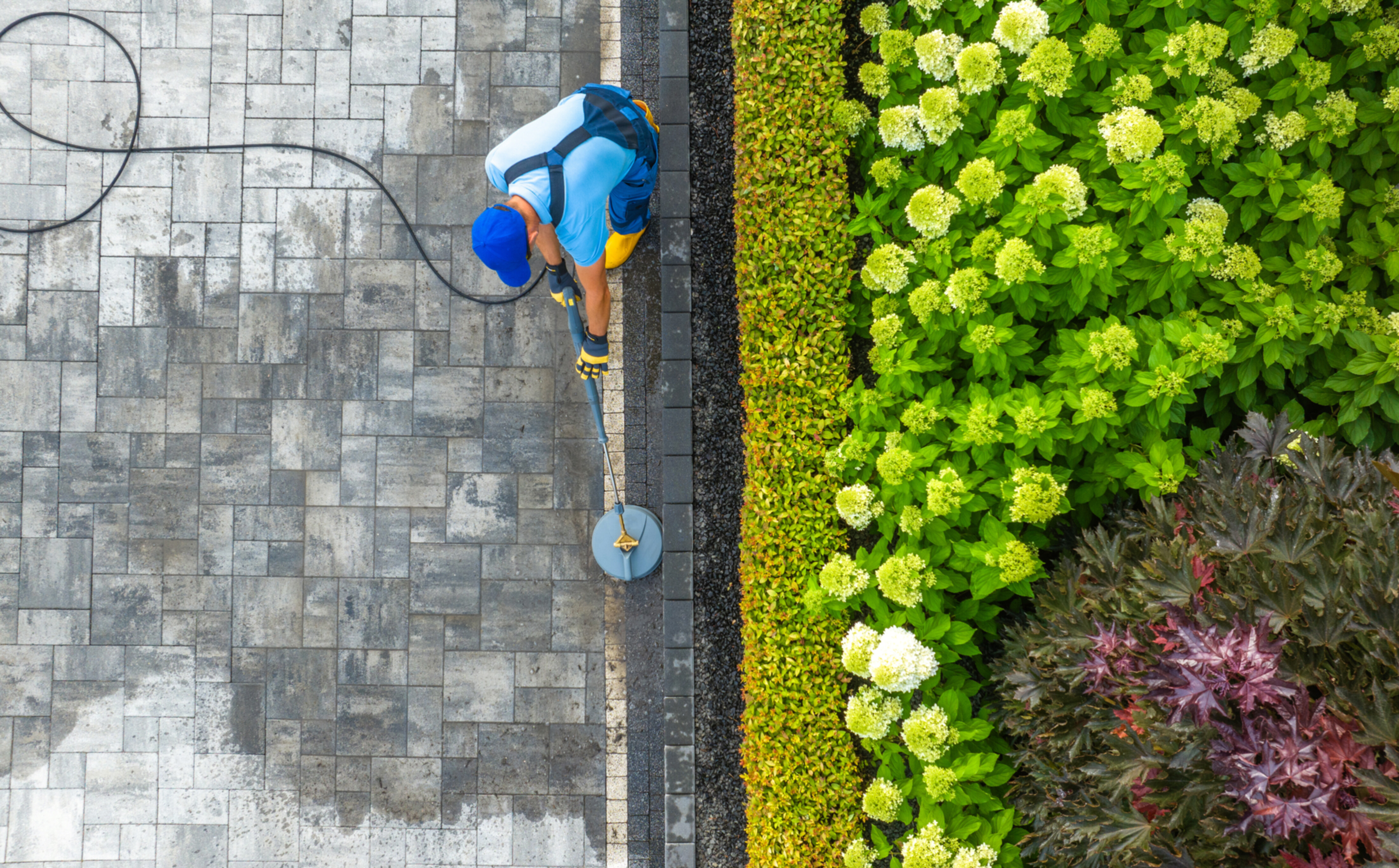 A bird's eye view image of a professional worker pressure washing a driveway.