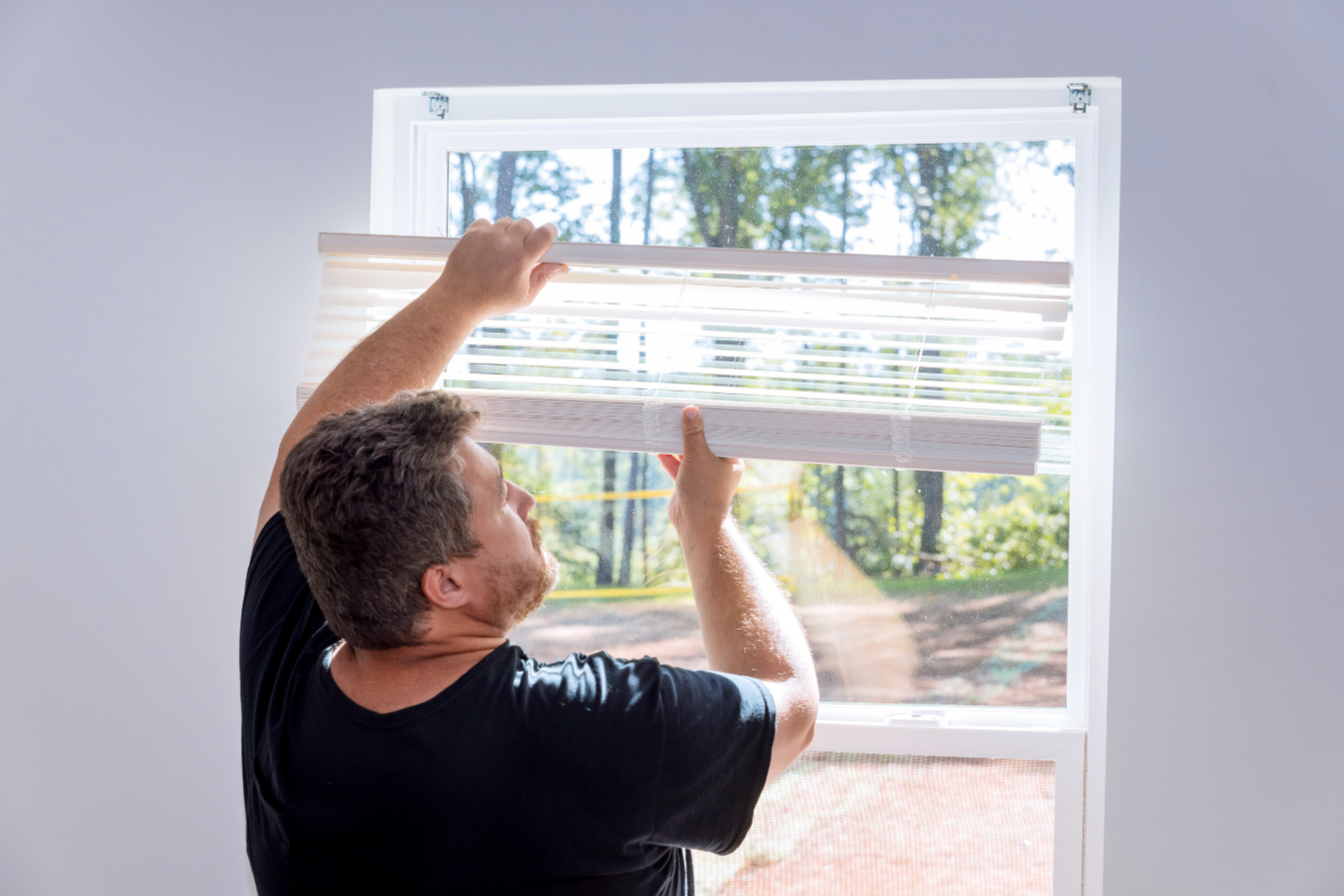 A handyman in the process of mounting and installing blinds.