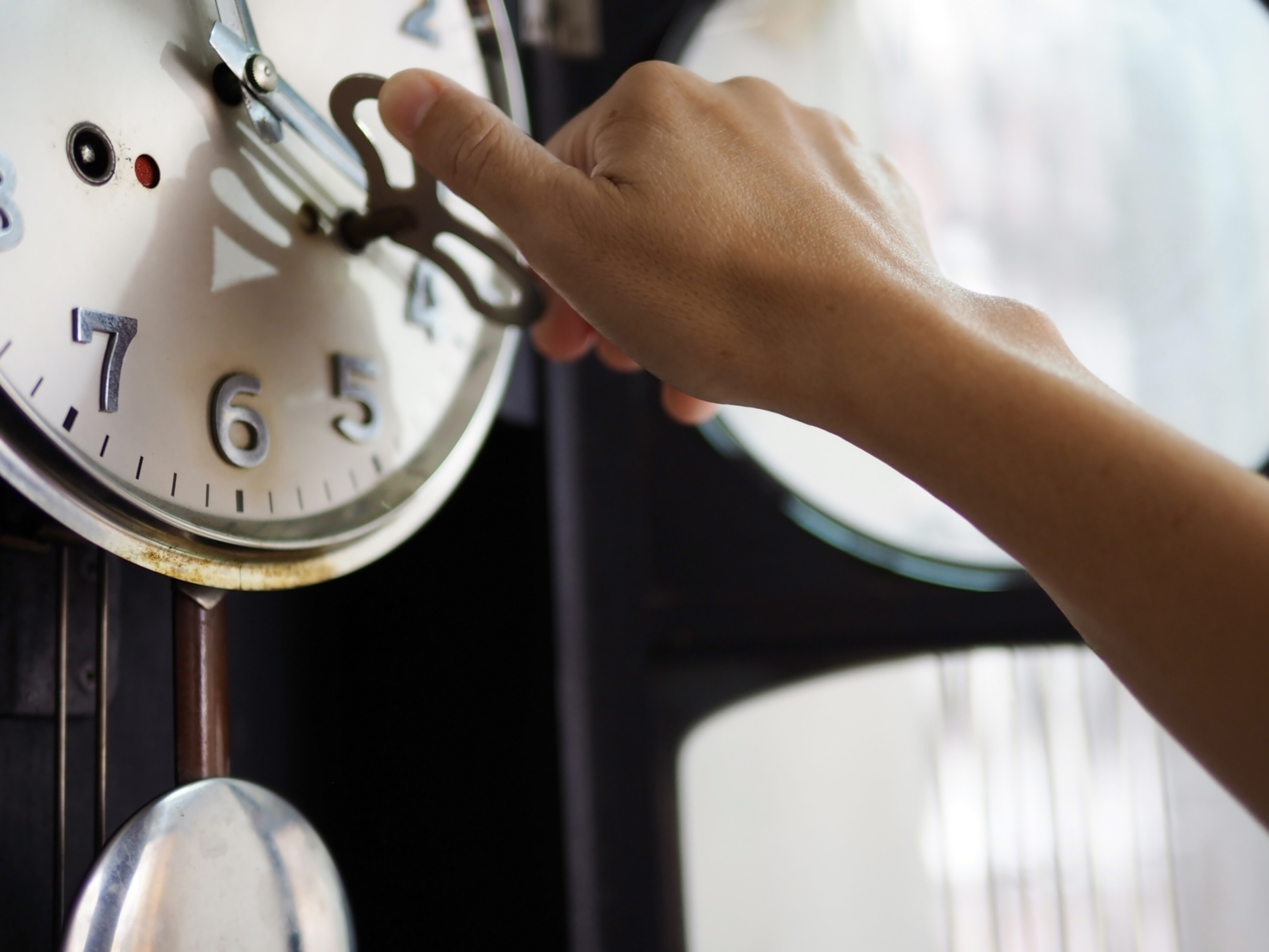 Male hand making adjustments to a clock during repair.