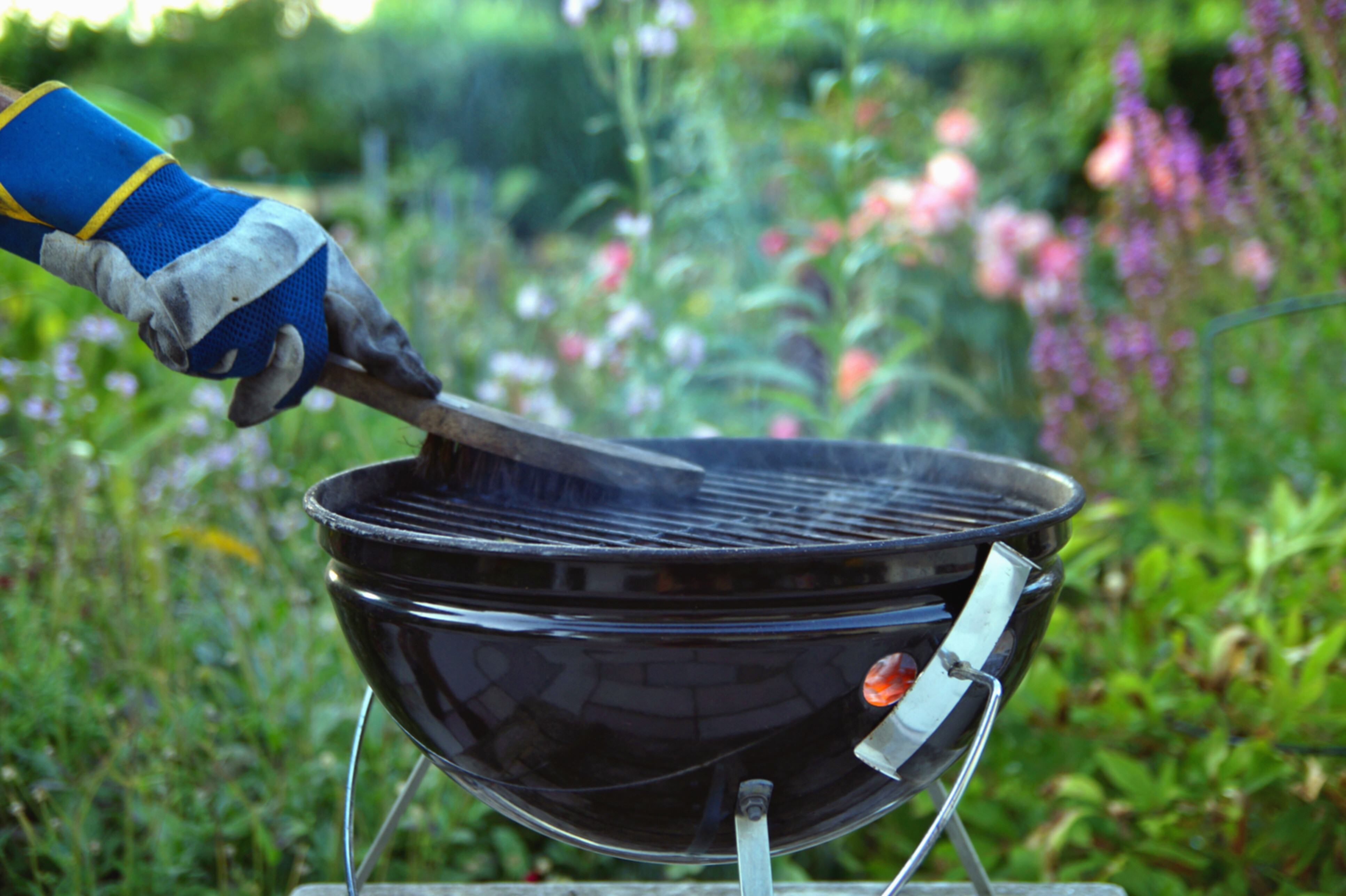 A gloved hand cleaning a bbq grill with a brush.