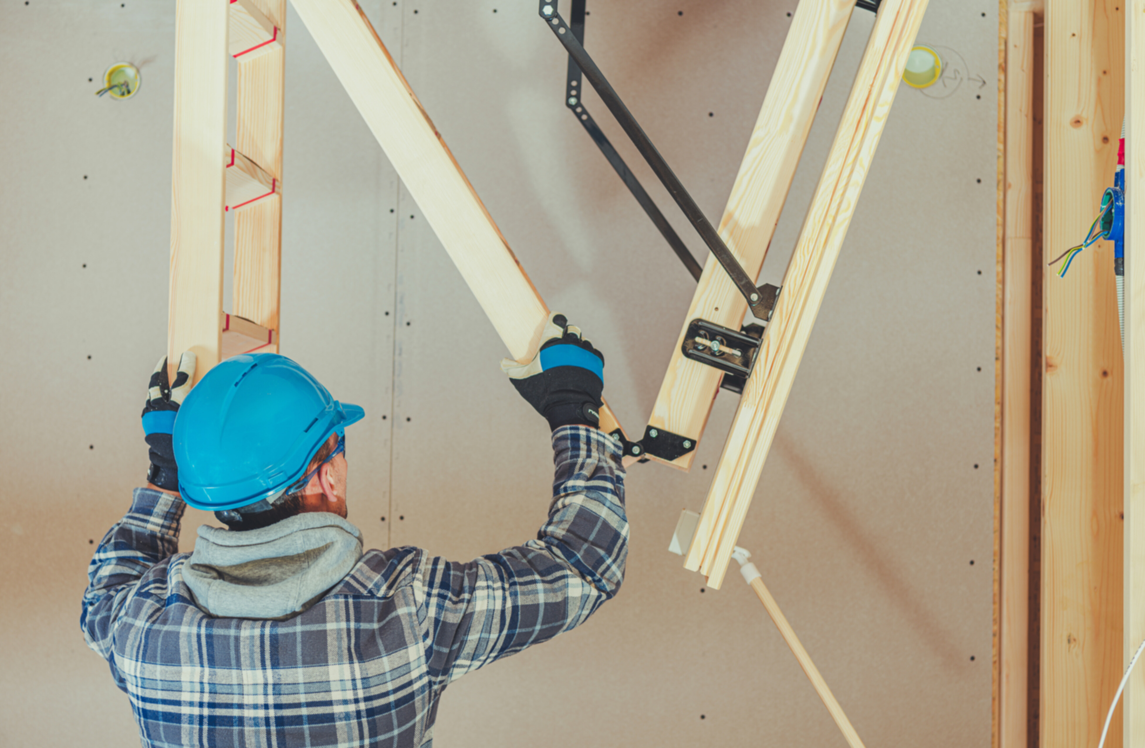 A caucassian handyman assembling a wooden attic ladder.