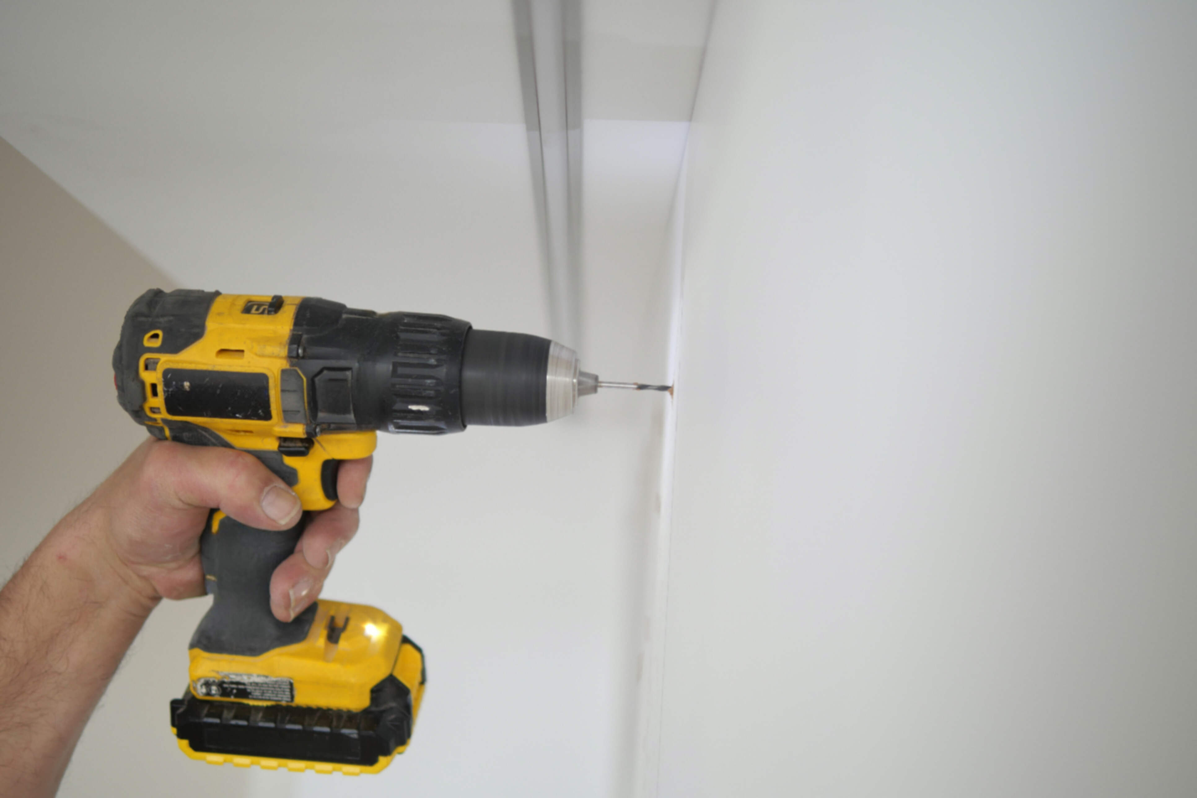 Male hands drilling holes inside a cabinet to install mounts for a Dyson.