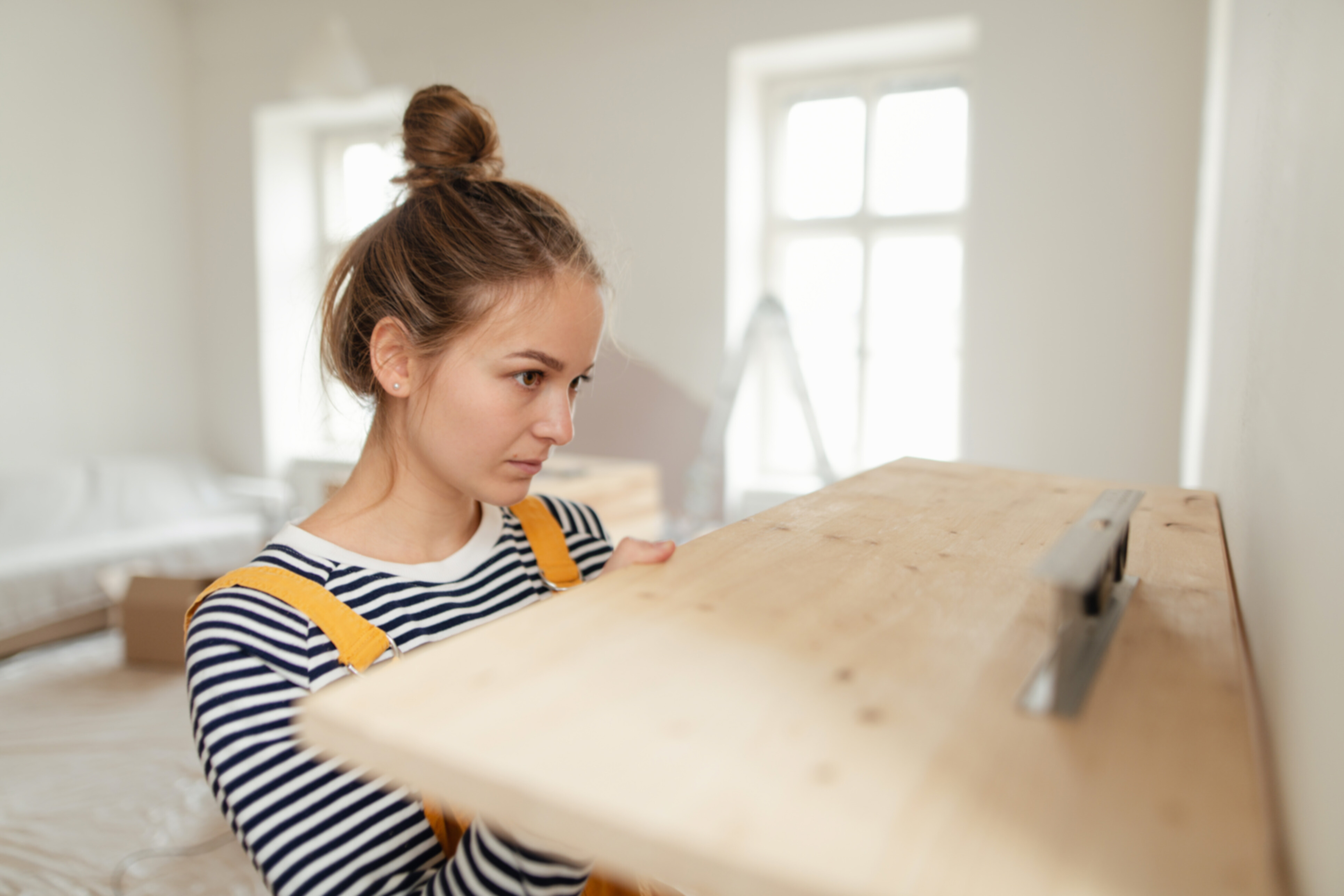 A caucasian woman hanging a wooden shelf in her bedroom.