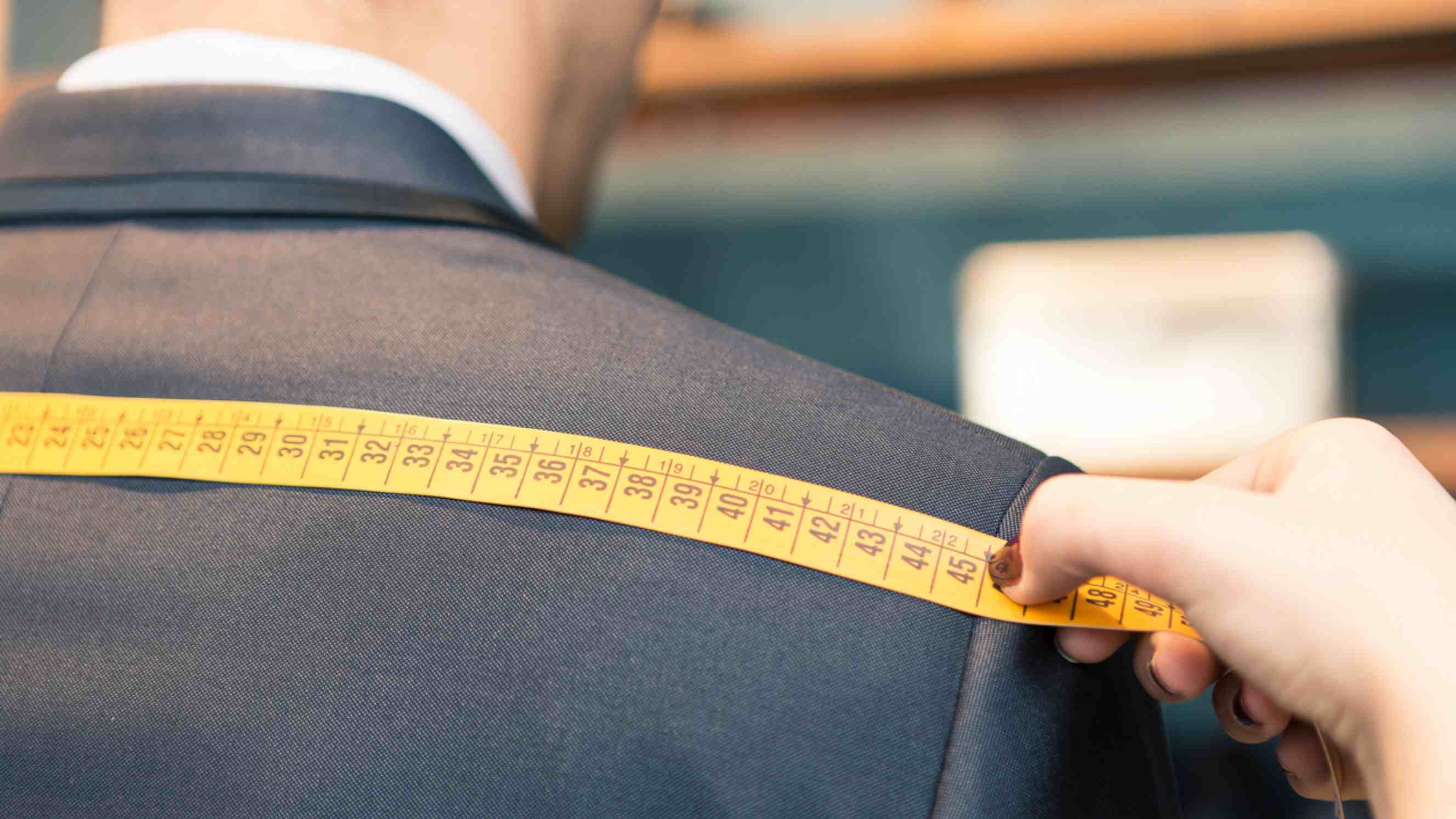 Made to measure vs bespoke - Detail of tailor's hands taking measurements for someone's suit