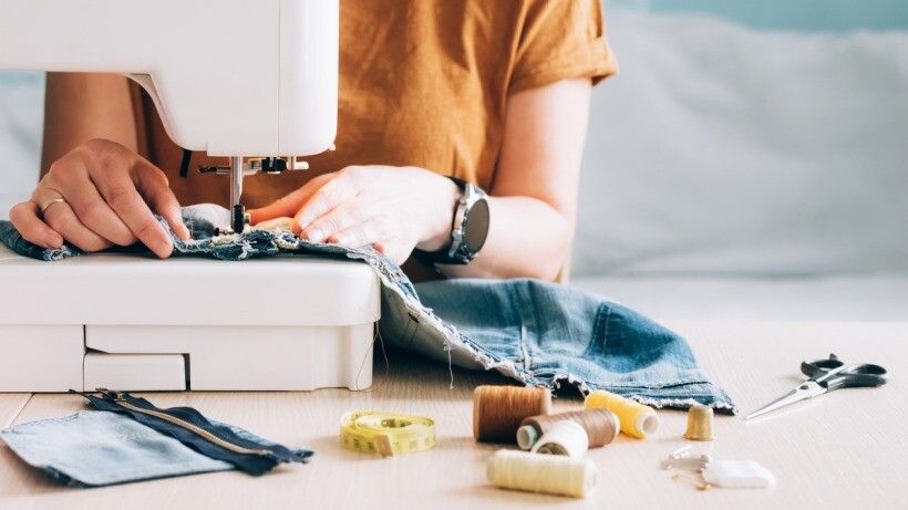 Hand sewing vs machine - A tailor using a sewing machine tao sew fabric from old denim clothes