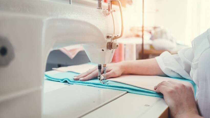 Hand sewing vs machine - A person sewing a blue fabric using a sewing machine in a design studio