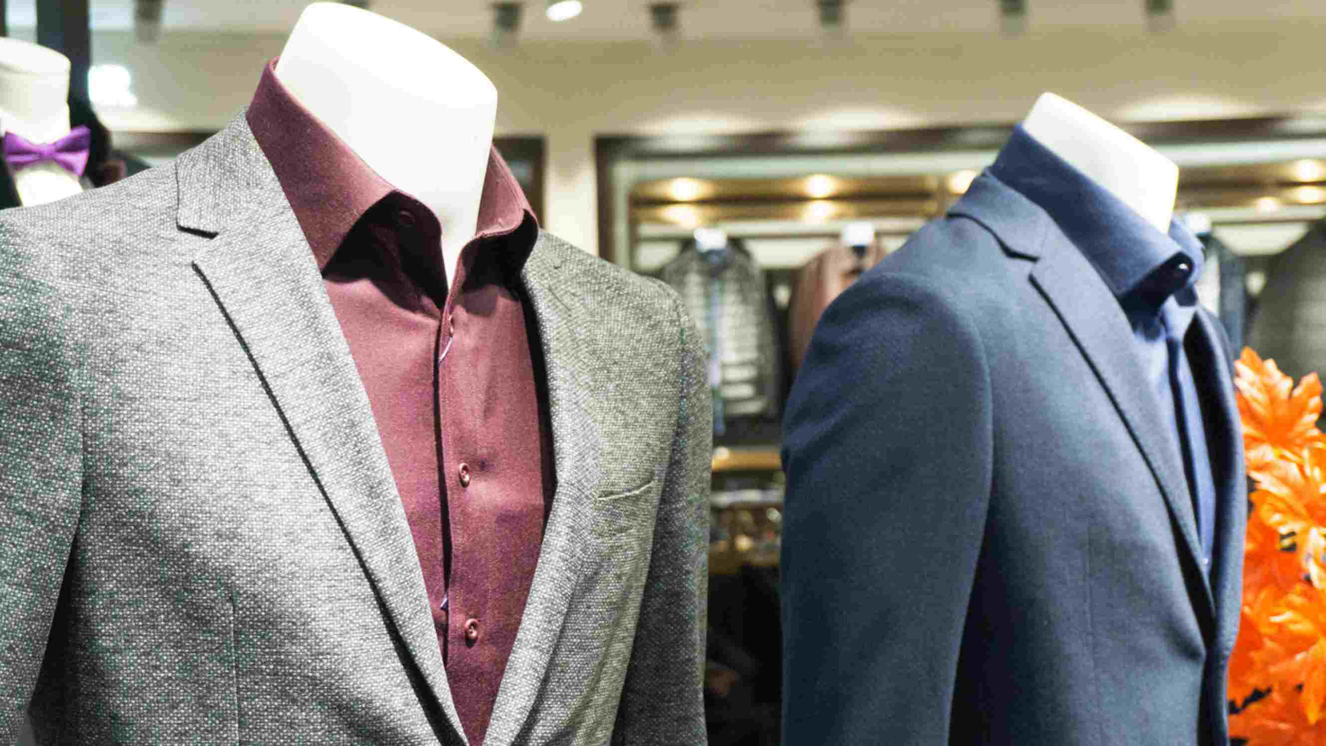 Tuxedo vs suit - Two mannequins wearing formal suits, one in a gray suit with a burgundy shirt and the other in a blue suit with a blue shirt