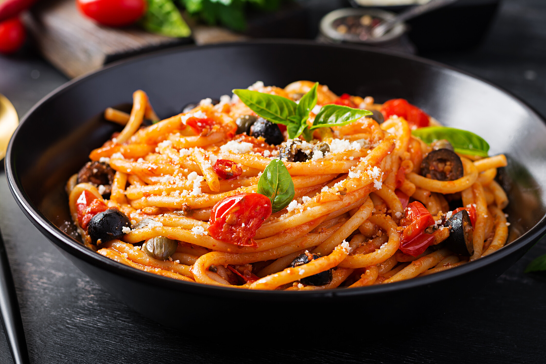 A bowl of pasta with tomatoes, olives, and basil, ready for delivery.