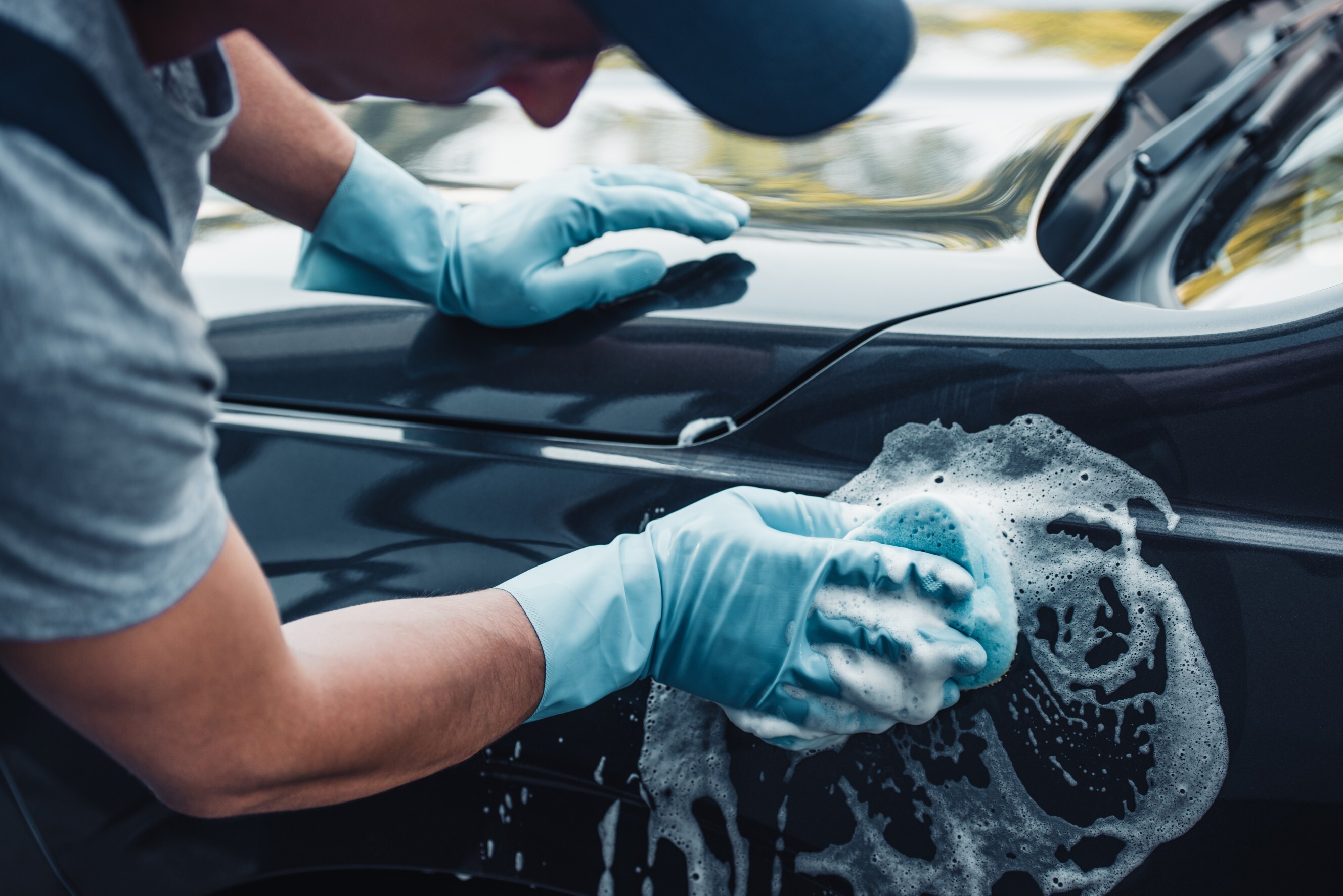 A person wearing gloves washing a car with soap and a sponge – a close-up shot of a car wash service. Find a professional car wash near me.