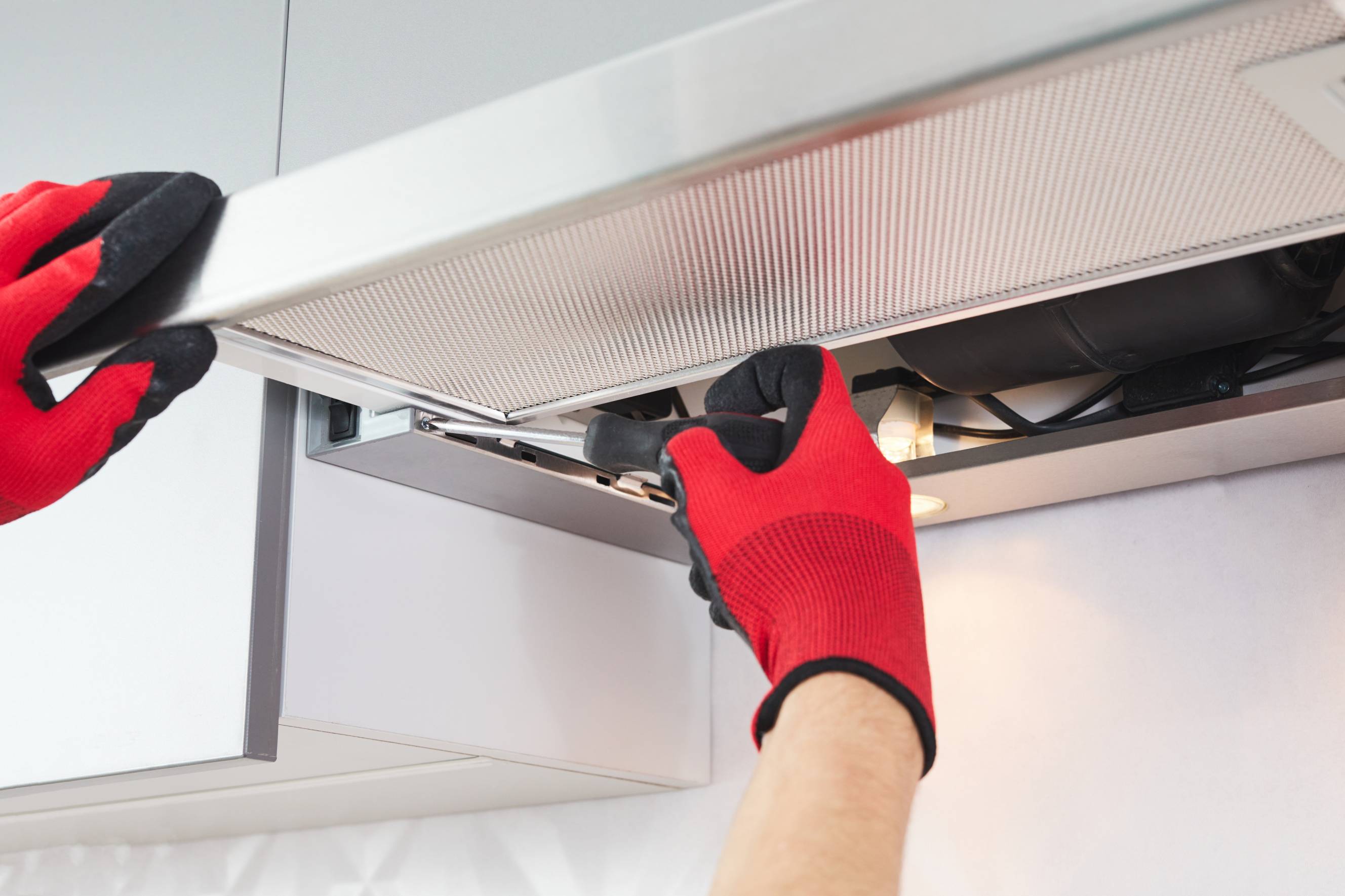 A technician doing cooker hood installation and repair for a white, modern kitchen. 