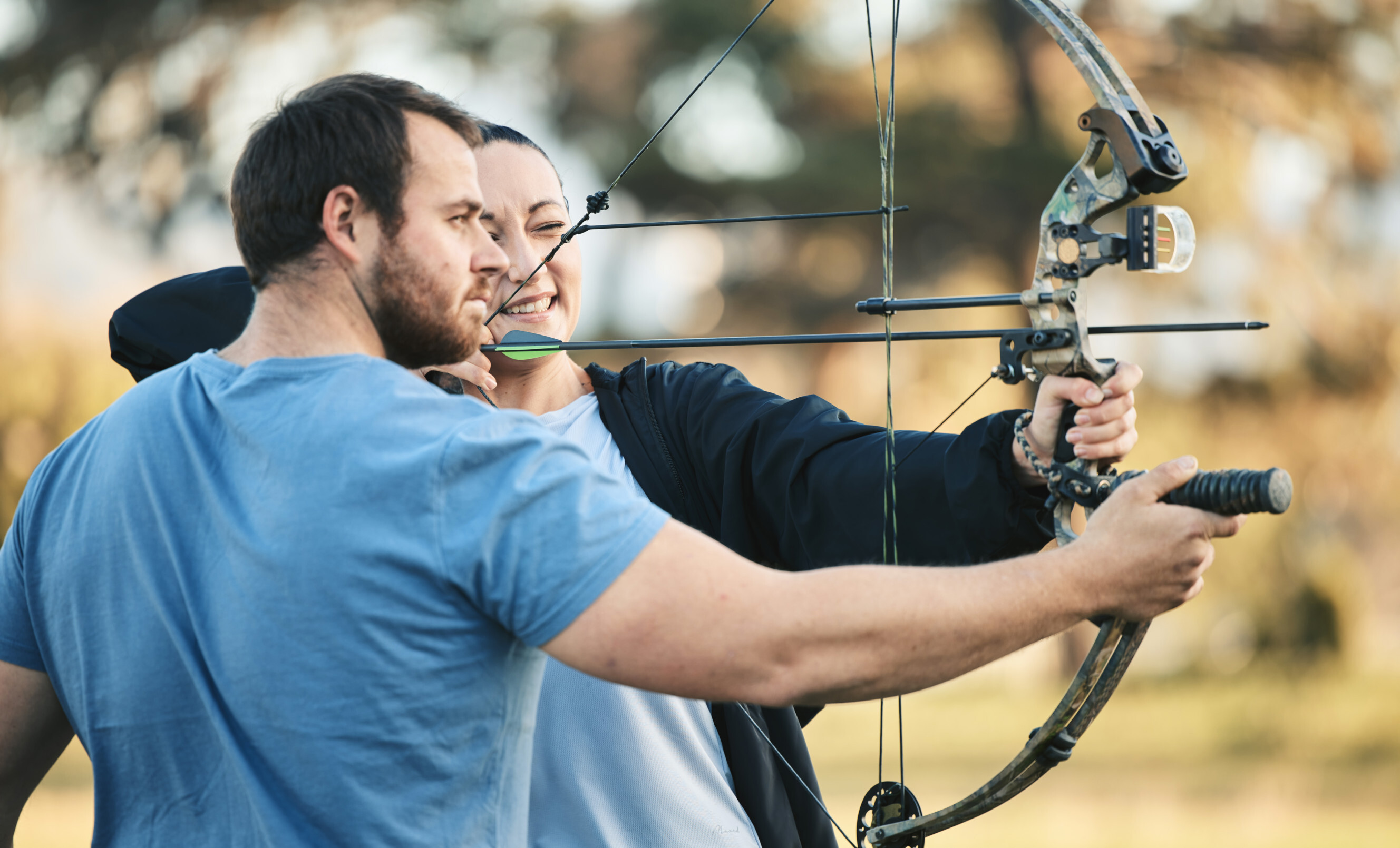 Archery instructor assisting a student with aiming a bow and arrow during an outdoor lesson