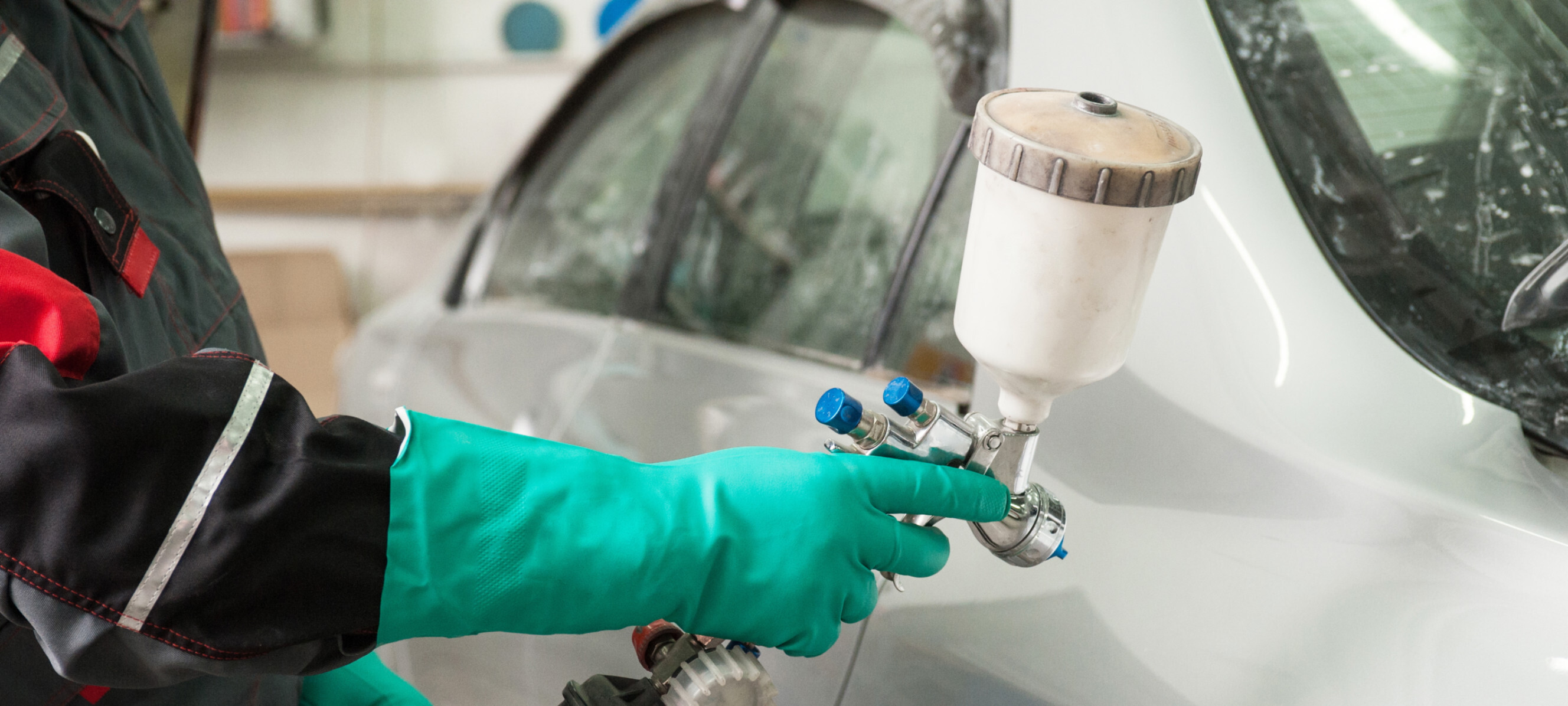 A person using a car paint spray tool to do a car respray on a white vehicle