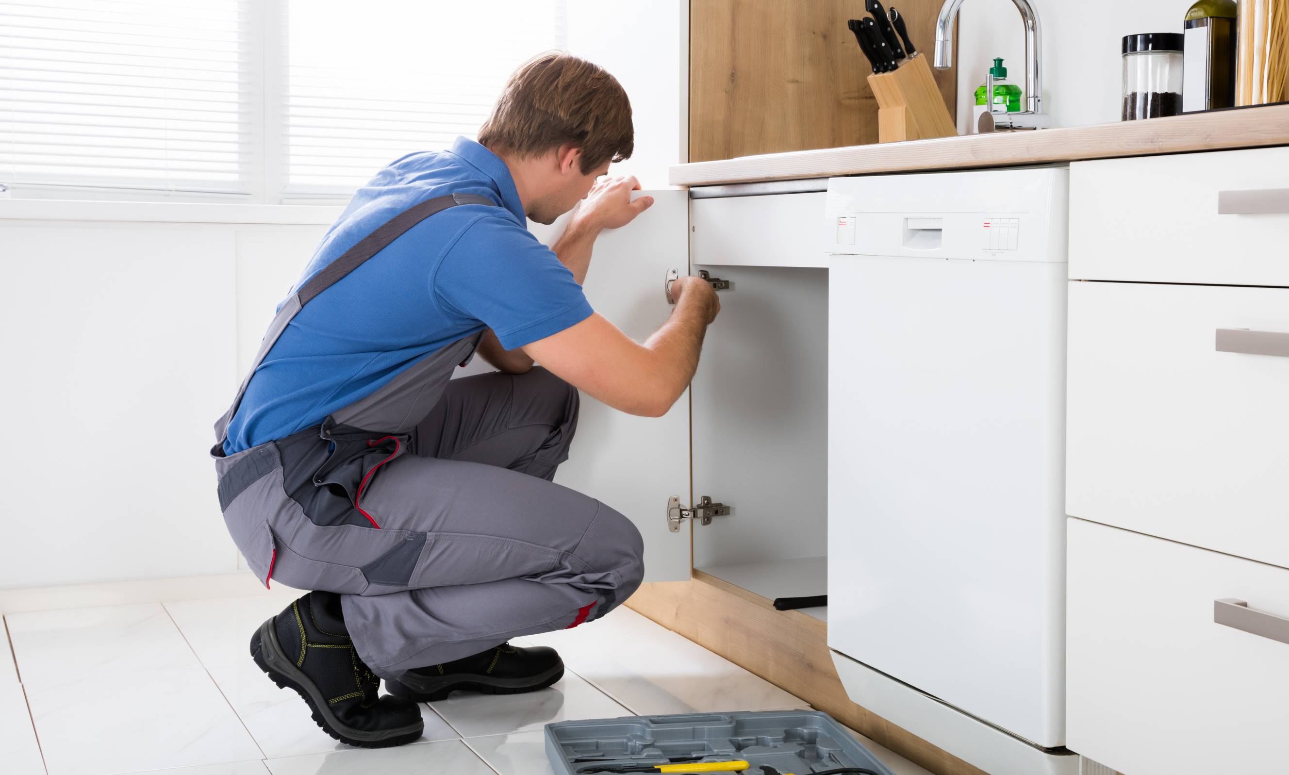 A carpenter installing a cabinet below a kitchen sink.