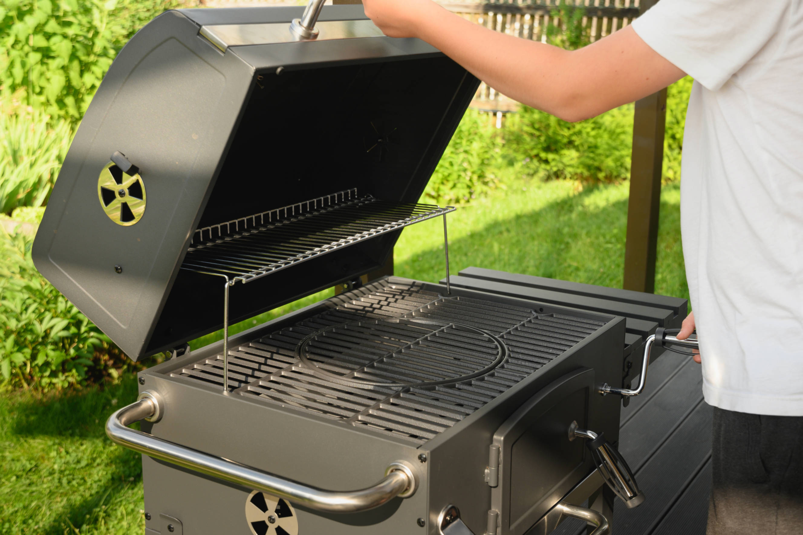 Person setting up a BBQ grill during a bbq assembly process, preparing the outdoor equipment for use in a garden setting.