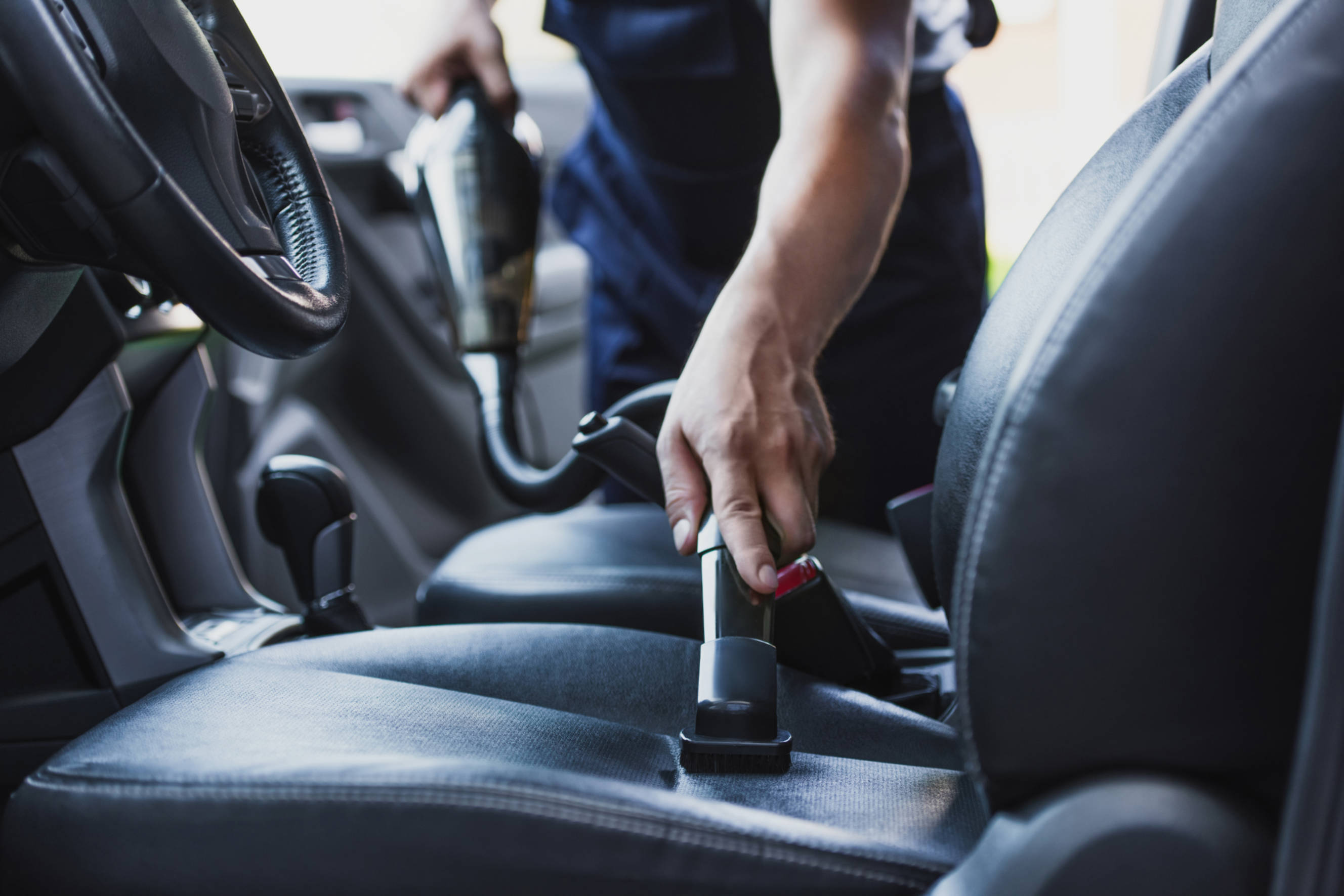 Technician performing car interior cleaning, vacuuming the seats and ensuring a thorough clean for the vehicle's interior.