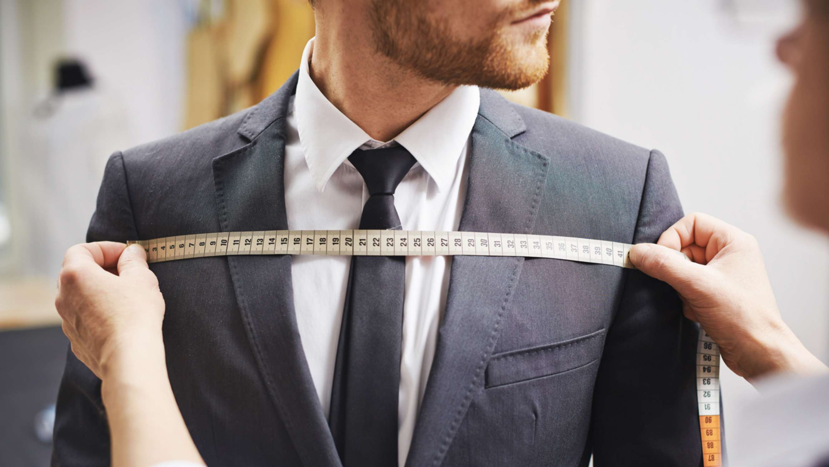 Tailored fit vs slim fit - Man in a suit being measured with a tape across his chest to determine the perfect fit