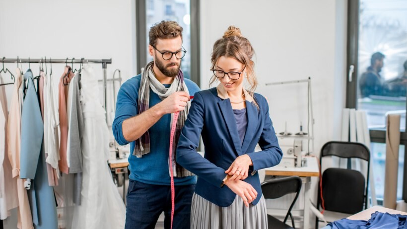 Tailored fit vs slim fit - A tailor measuring jacket on a client standing at the studio 