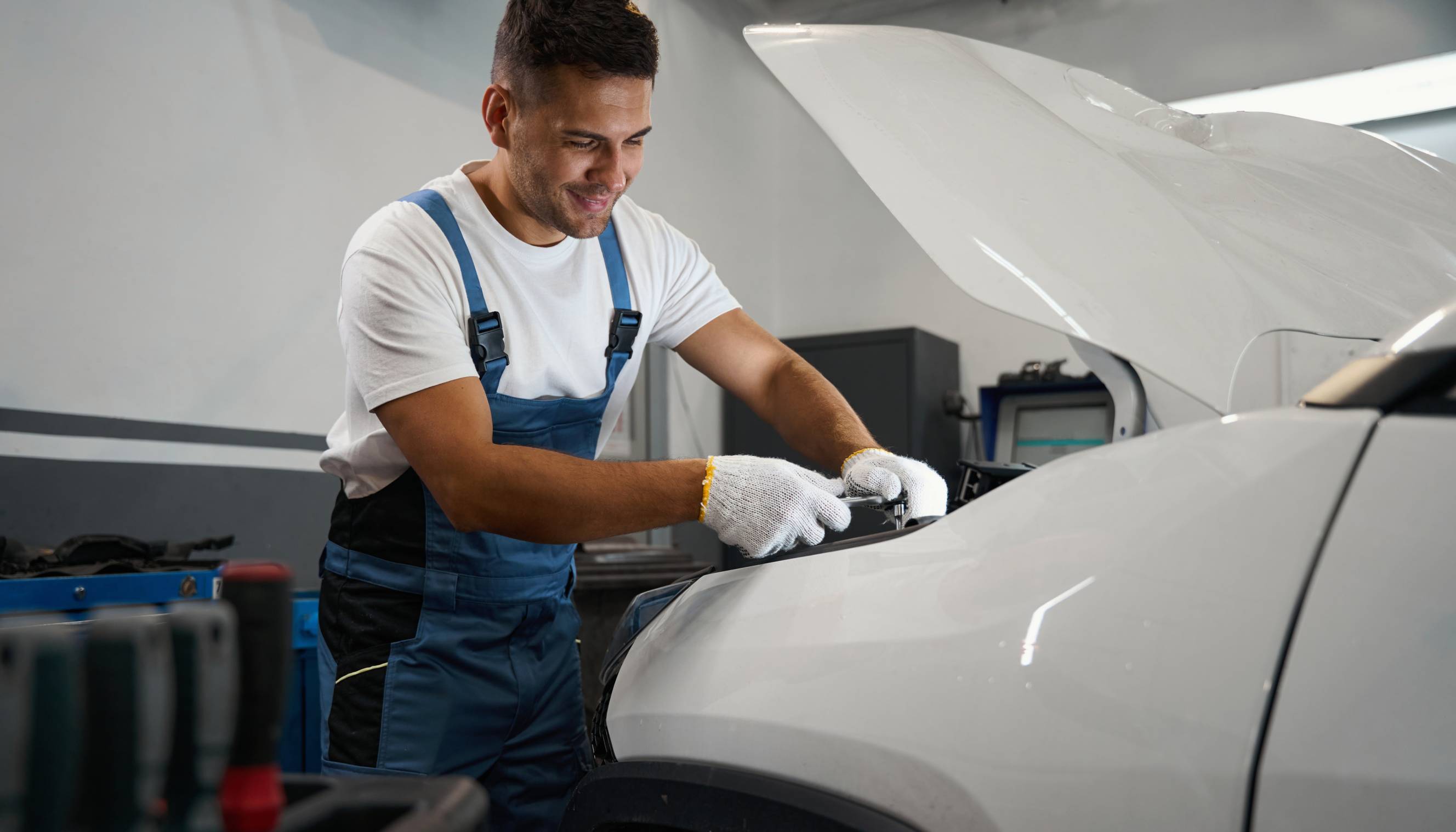 An auto electrician performing an electric car service under the hood in a workshop.