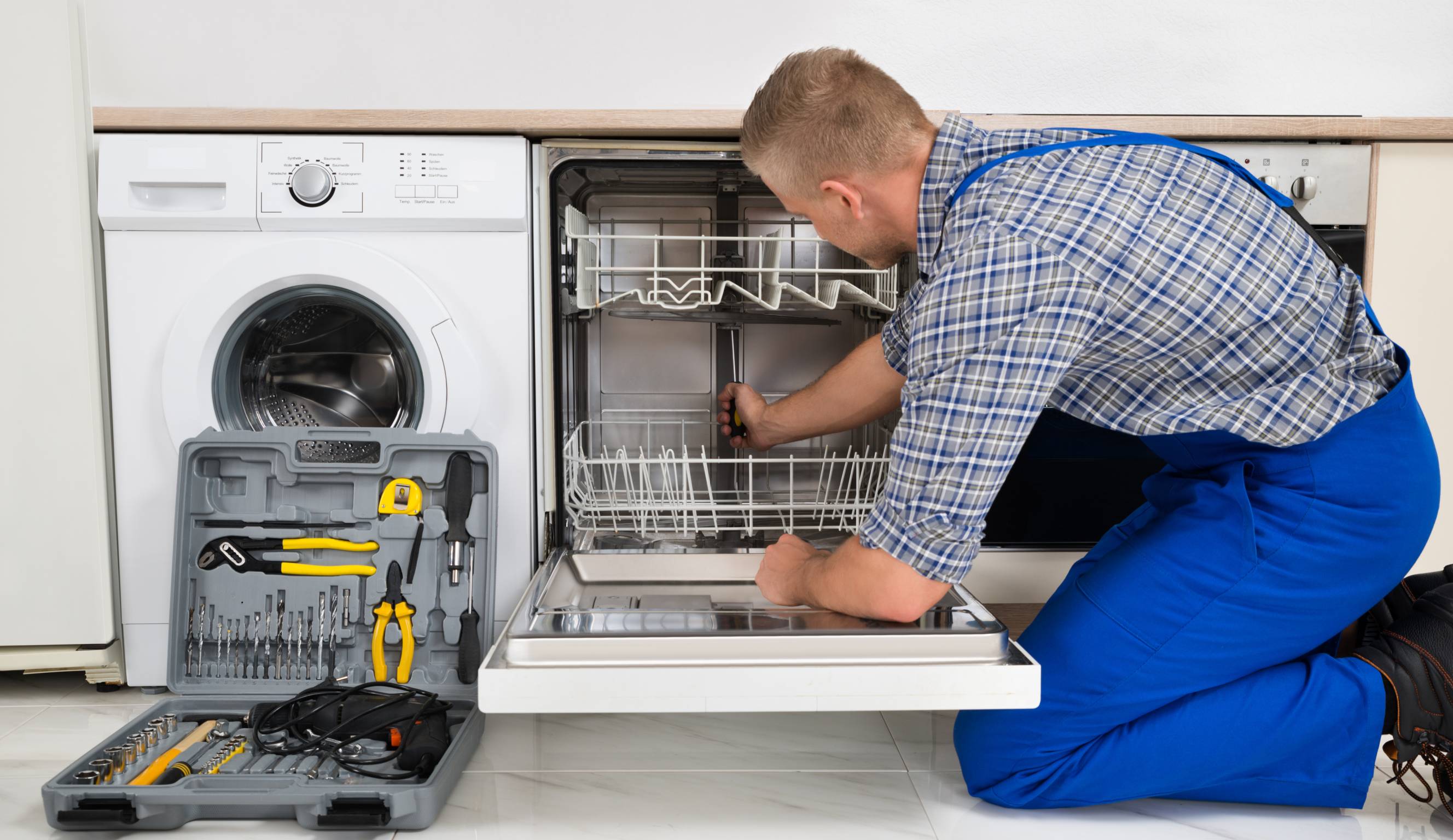 A technician performing dishwasher repair with a toolkit in a modern kitchen.