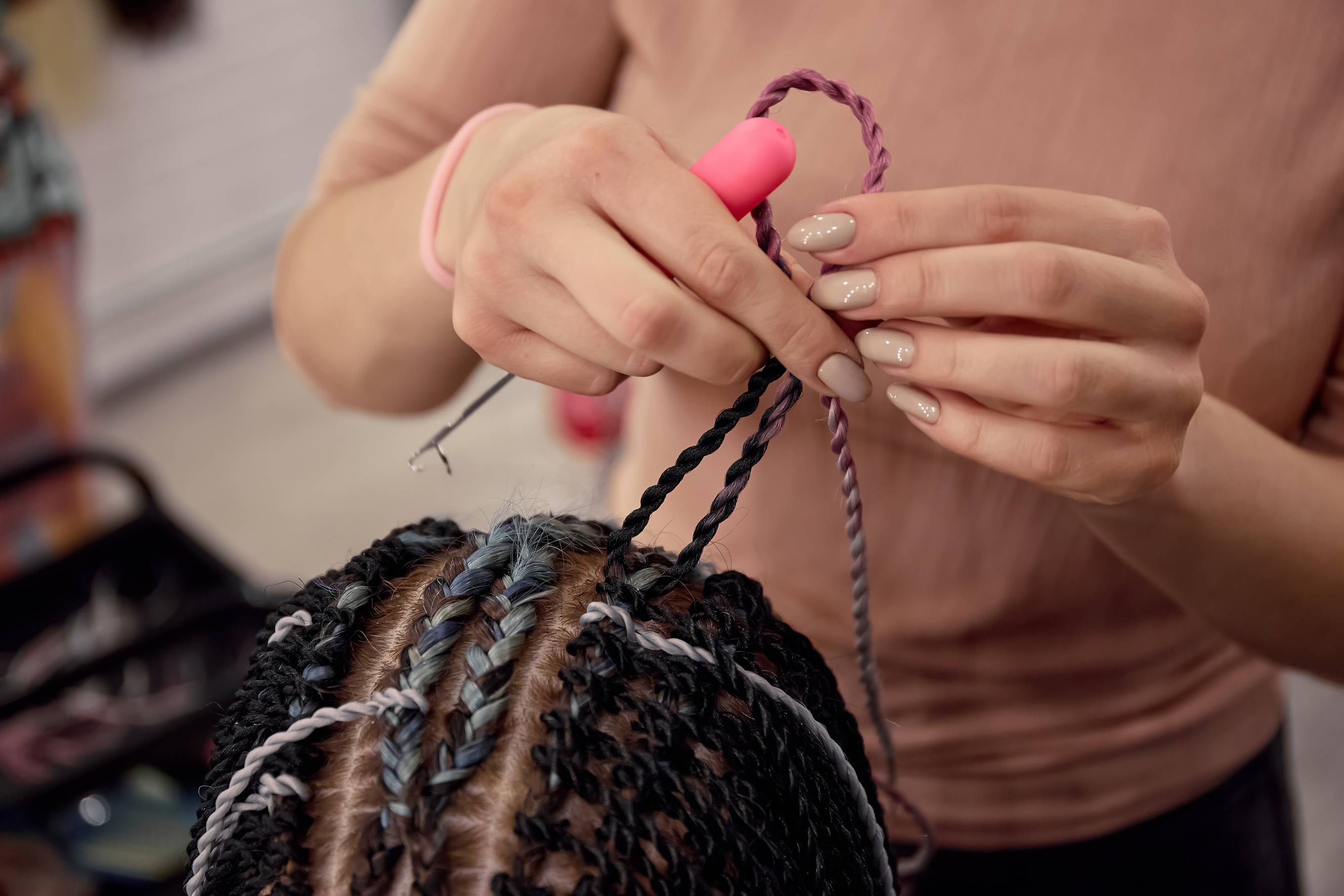 A stylist specialising in hair braiding carefully braiding a client's dark, curly hair in a salon setting.