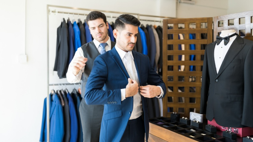 Tailored fit vs slim fit - Two persons in a clothing store, one of whom is trying on a tailored fit blue suit jacket