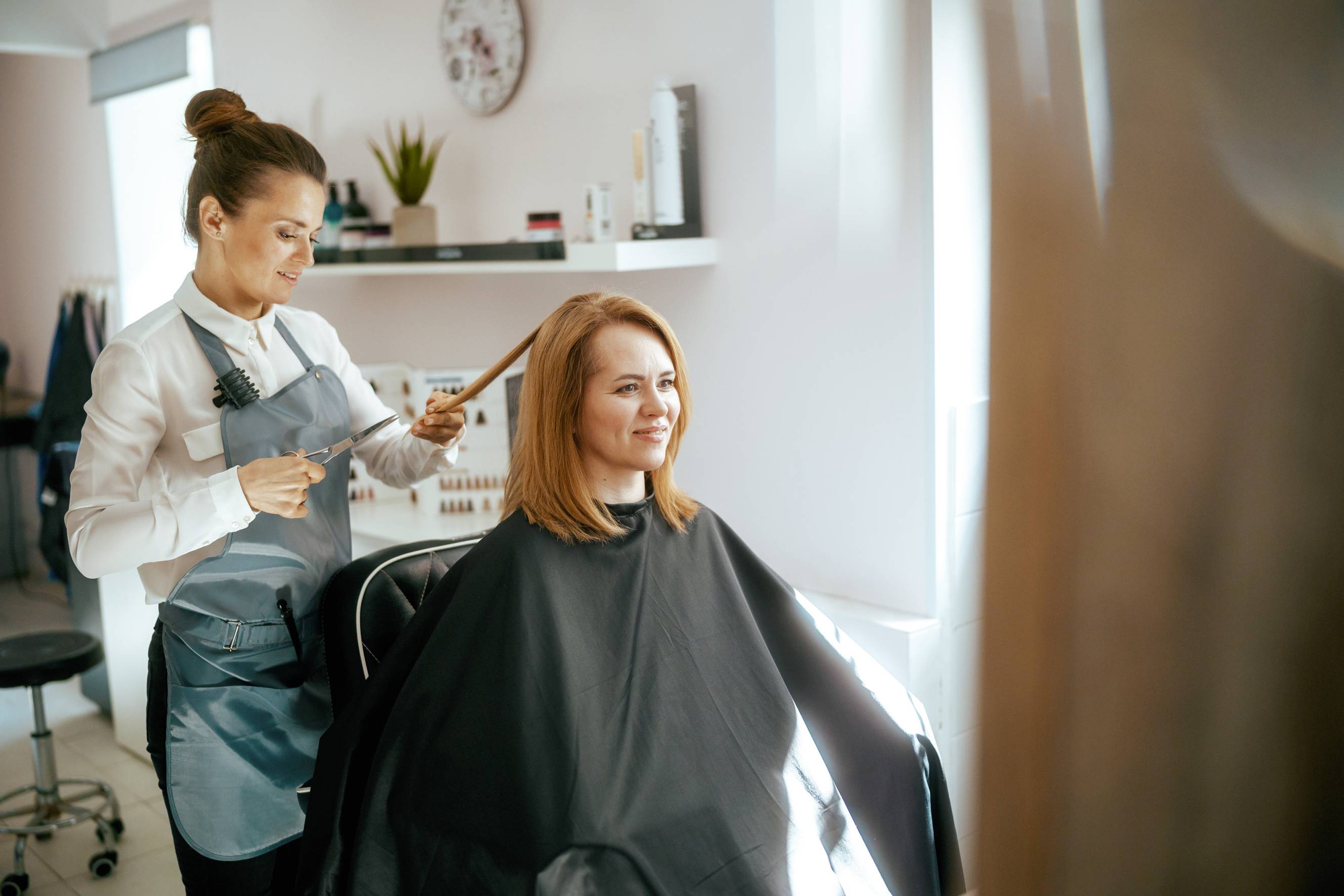 A female hair stylist trimming a client's hair in a salon setting. 